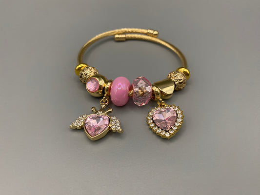 “Belle Pink Charm Bracelet with gold-plated finish, featuring heart-cut crystals and rhinestones. Made from durable stainless steel with playful charms and micro insert inlay technology.”