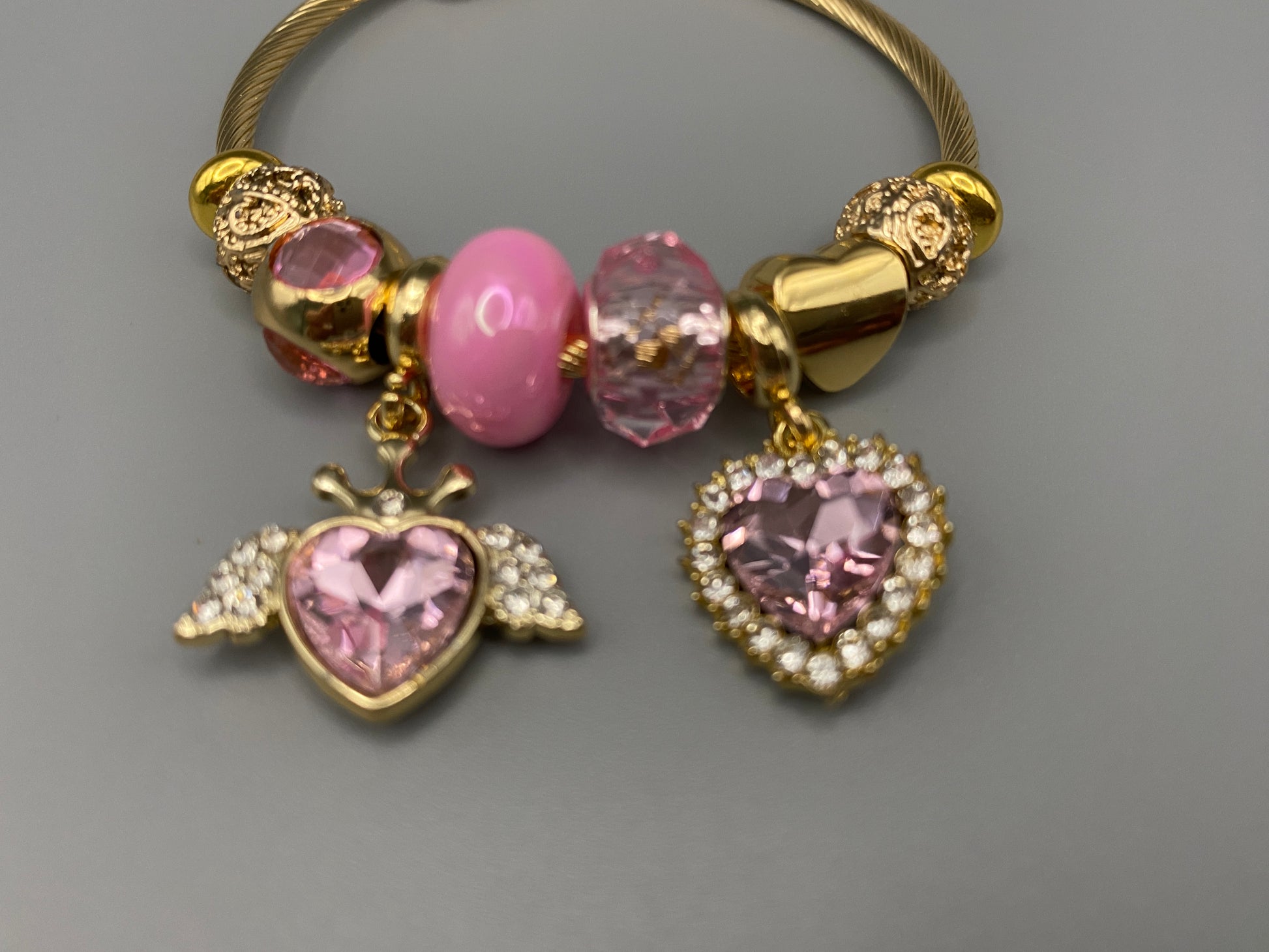 “Belle Pink Charm Bracelet with gold-plated finish, featuring heart-cut crystals and rhinestones. Made from durable stainless steel with playful charms and micro insert inlay technology.”