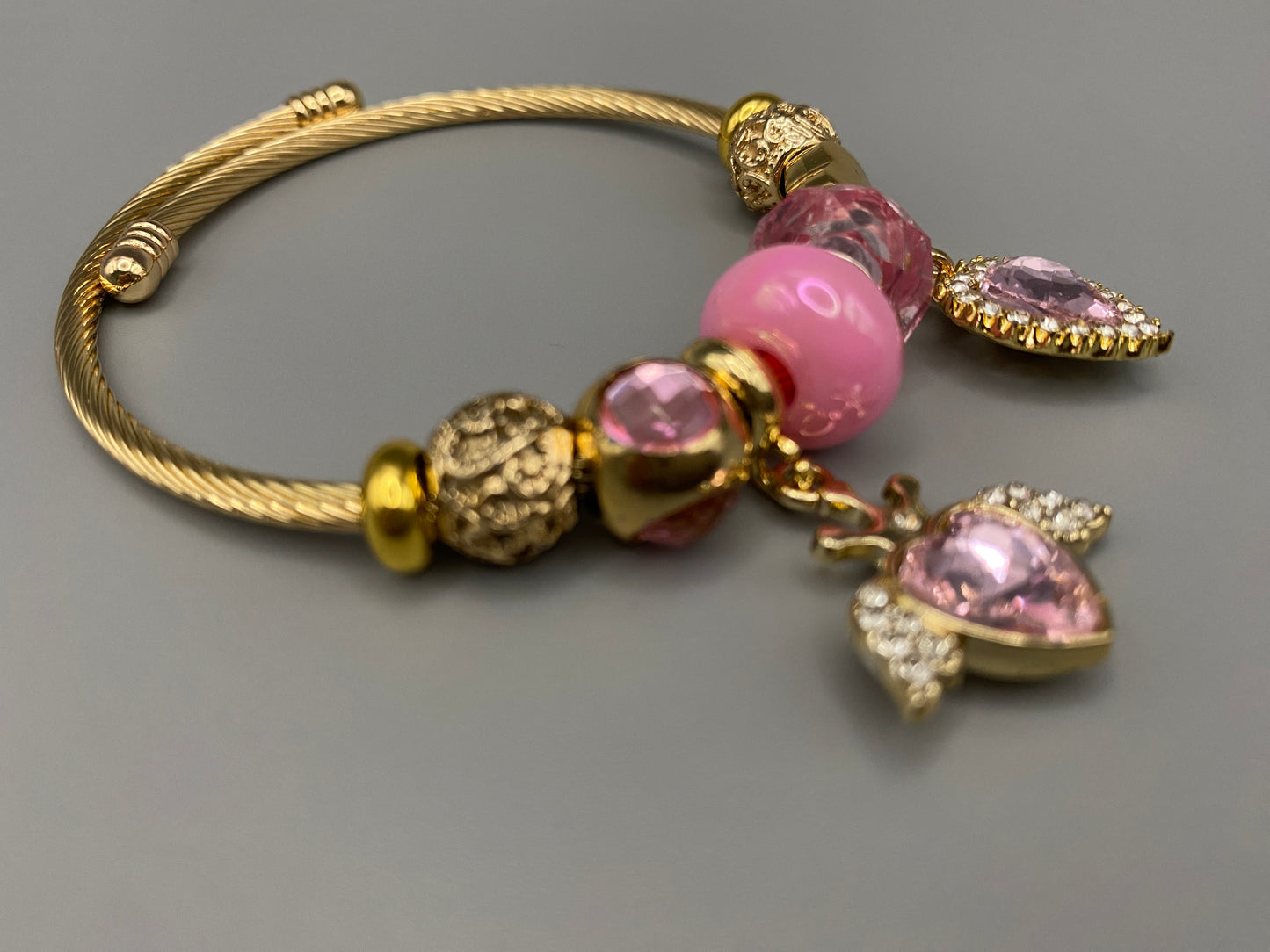 “Belle Pink Charm Bracelet with gold-plated finish, featuring heart-cut crystals and rhinestones. Made from durable stainless steel with playful charms and micro insert inlay technology.”