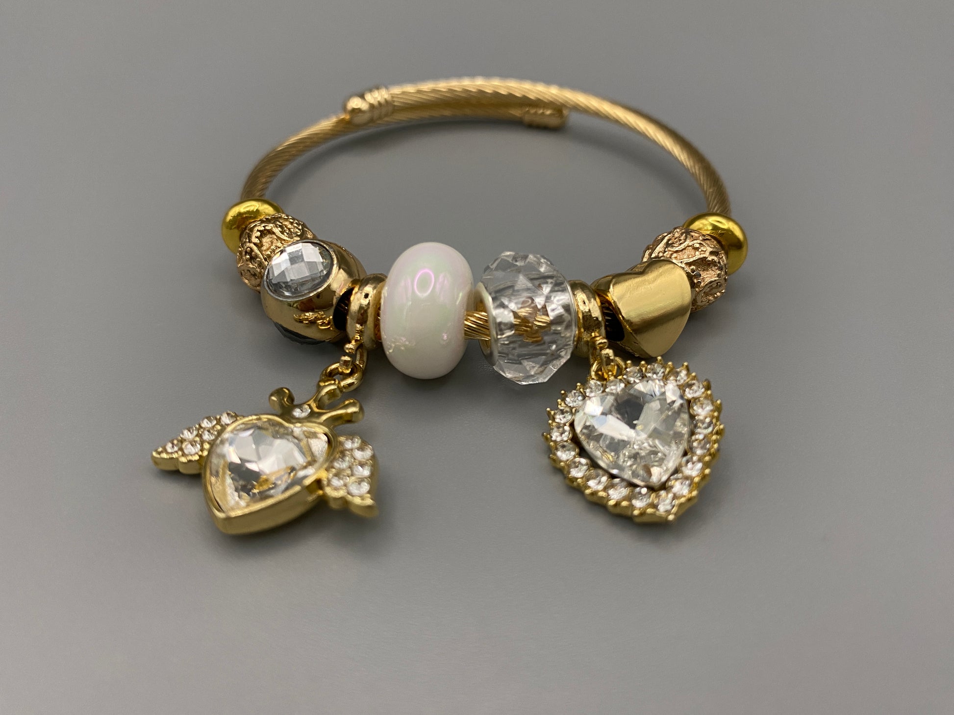“Belle White Charm Bracelet with gold-plated finish, featuring heart-cut crystals and rhinestones. Made from durable stainless steel with playful charms and micro insert inlay technology.”