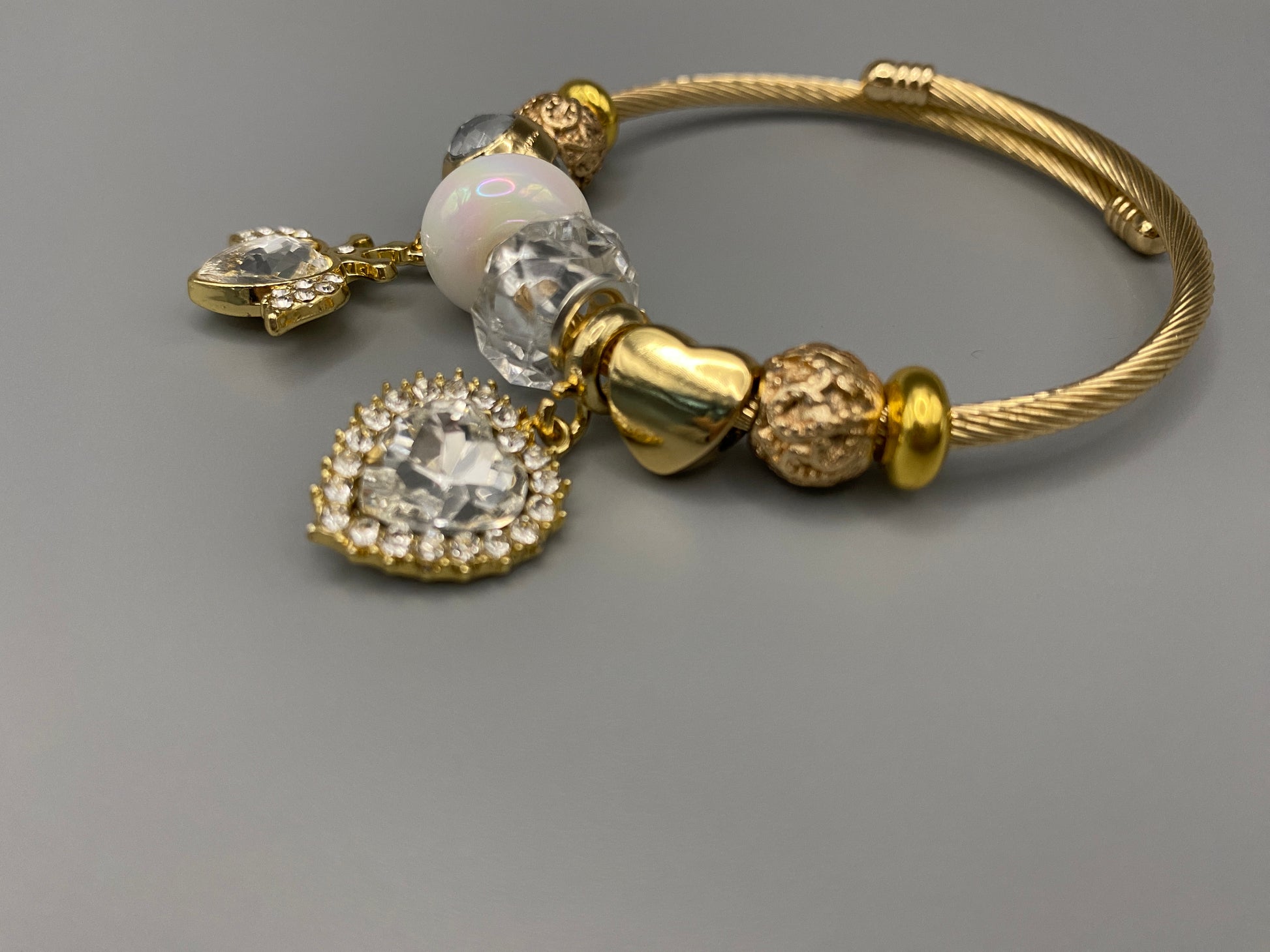 “Belle White Charm Bracelet with gold-plated finish, featuring heart-cut crystals and rhinestones. Made from durable stainless steel with playful charms and micro insert inlay technology.”