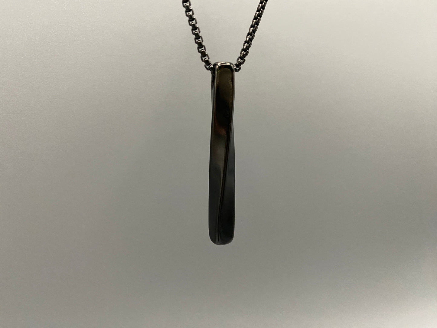 "Stainless steel twist pendant necklaces available in black gun plated, gold plated, and titanium plated finishes, displayed on a dark background. Each necklace features a geometric twist pendant on a link chain, suitable for unisex wear.”