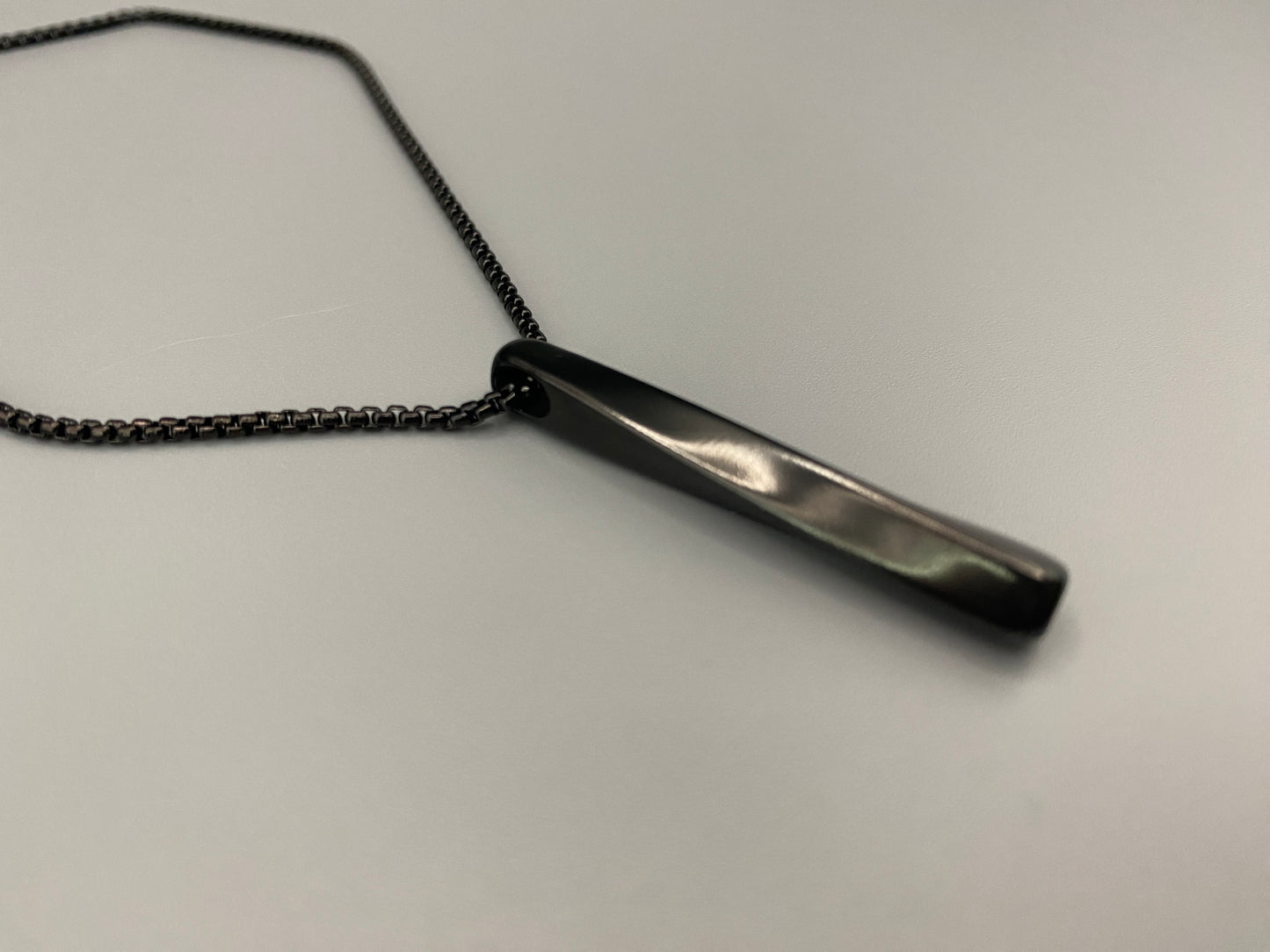 "Stainless steel twist pendant necklaces available in black gun plated, gold plated, and titanium plated finishes, displayed on a dark background. Each necklace features a geometric twist pendant on a link chain, suitable for unisex wear.”