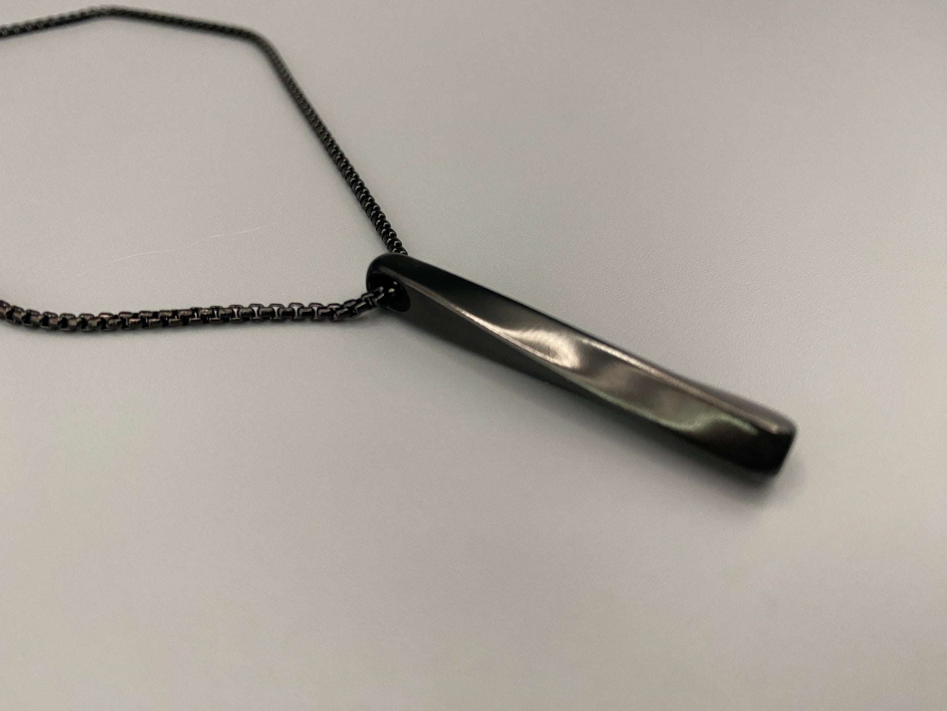 "Stainless steel twist pendant necklaces available in black gun plated, gold plated, and titanium plated finishes, displayed on a dark background. Each necklace features a geometric twist pendant on a link chain, suitable for unisex wear.”