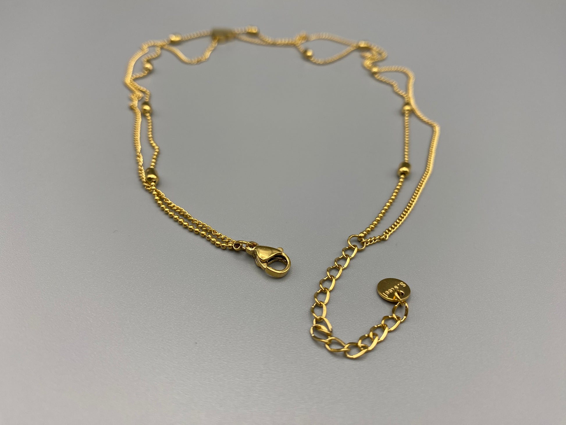 Cora, This exquisite necklace is crafted from luxurious 18K gold, featuring a unique twin chain design. One chain is adorned with delicate beads, while the other showcases a charming heart-shaped pendant.