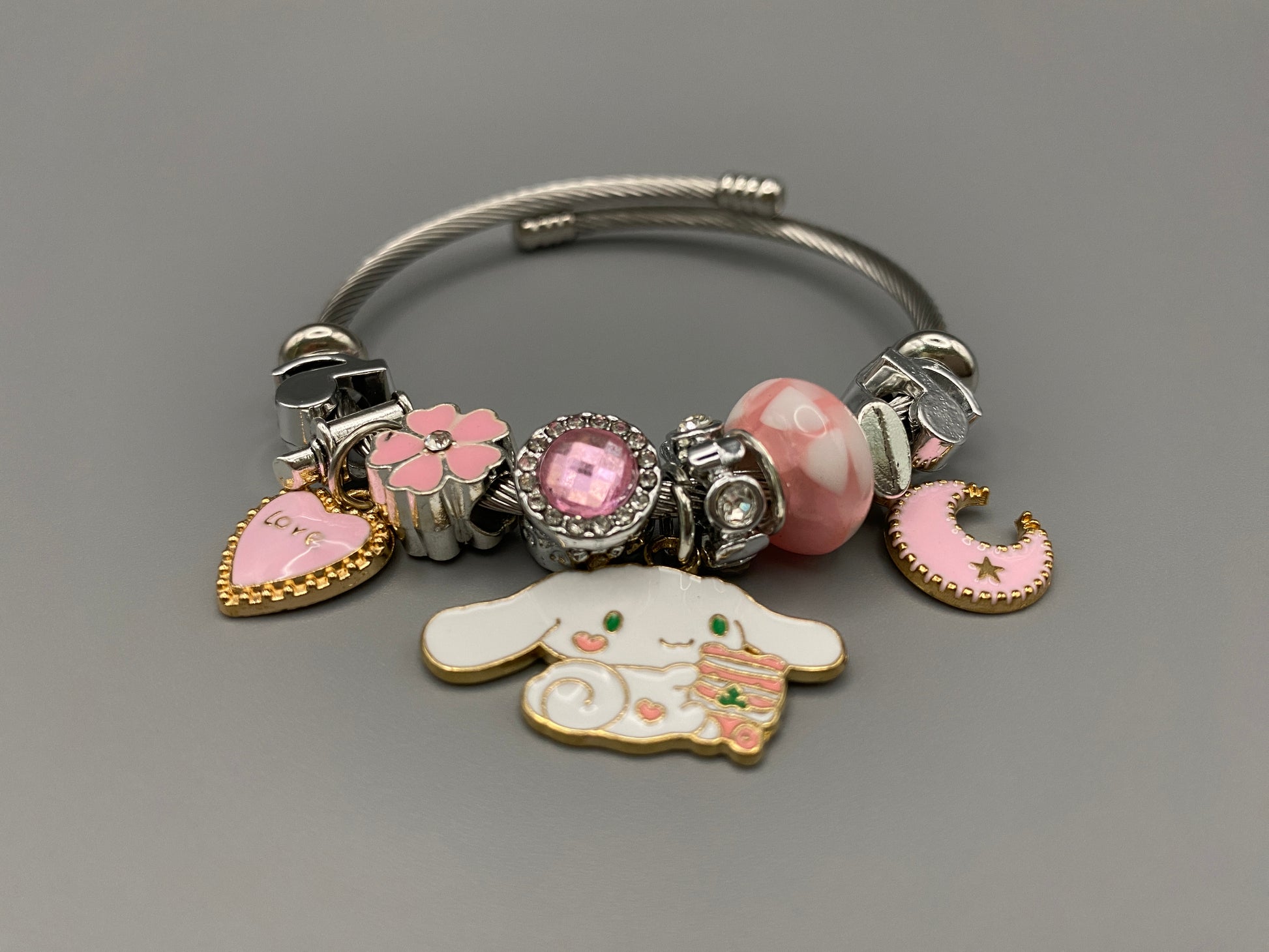 “Cartoon Character Charm Bracelet Bangle in Pink. This charming bracelet features stainless steel bangles adorned with alloy charms, crystals, and glass beads. High-quality materials ensure durability, while the adorable design with pink accents adds a playful elegance. Perfect for everyday wear or special occasions.”