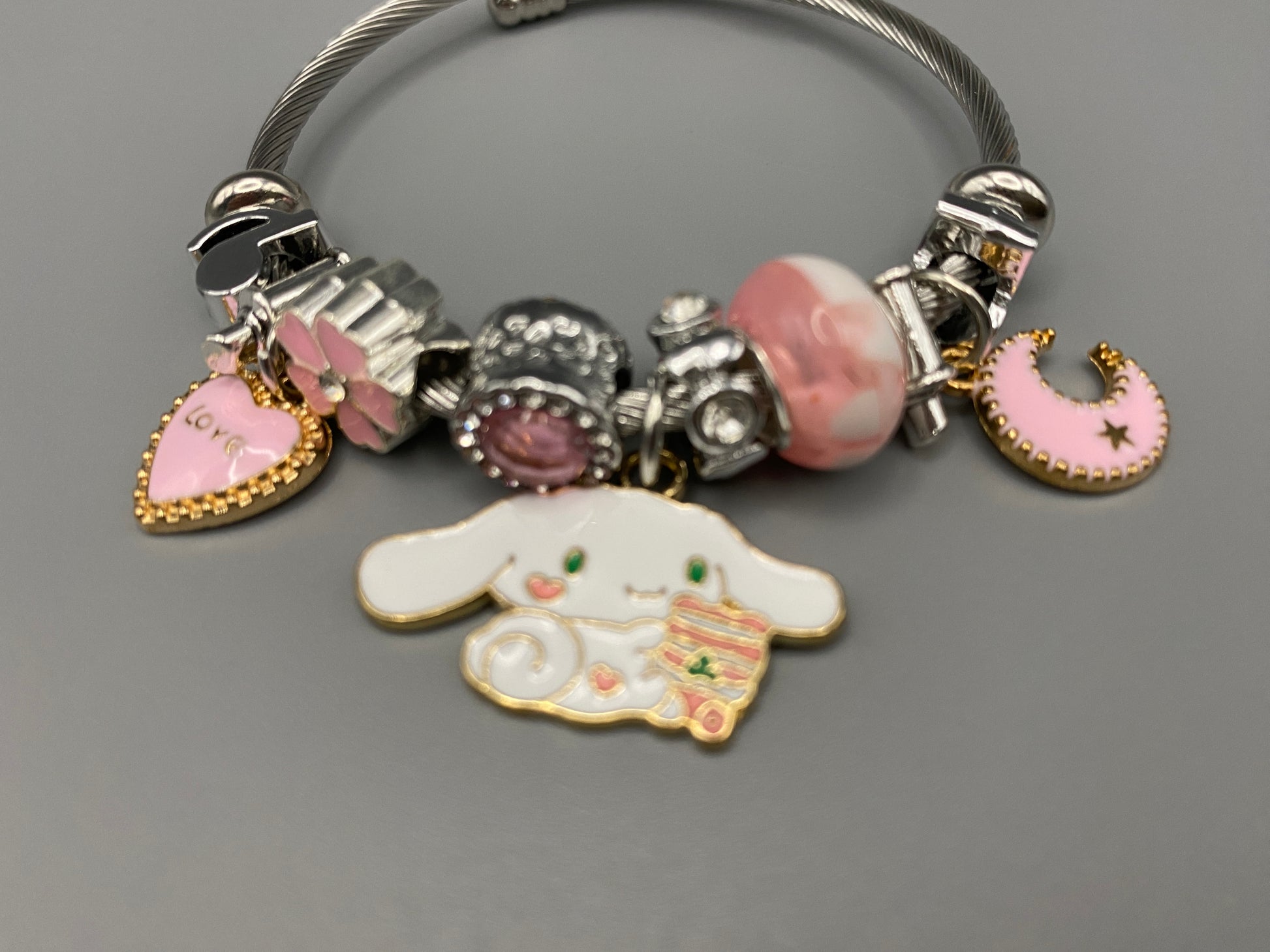“Cartoon Character Charm Bracelet Bangle in Pink. This charming bracelet features stainless steel bangles adorned with alloy charms, crystals, and glass beads. High-quality materials ensure durability, while the adorable design with pink accents adds a playful elegance. Perfect for everyday wear or special occasions.”