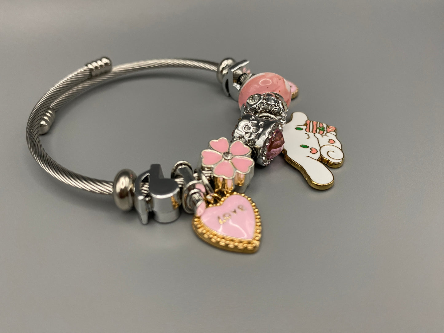 “Cartoon Character Charm Bracelet Bangle in Pink. This charming bracelet features stainless steel bangles adorned with alloy charms, crystals, and glass beads. High-quality materials ensure durability, while the adorable design with pink accents adds a playful elegance. Perfect for everyday wear or special occasions.”