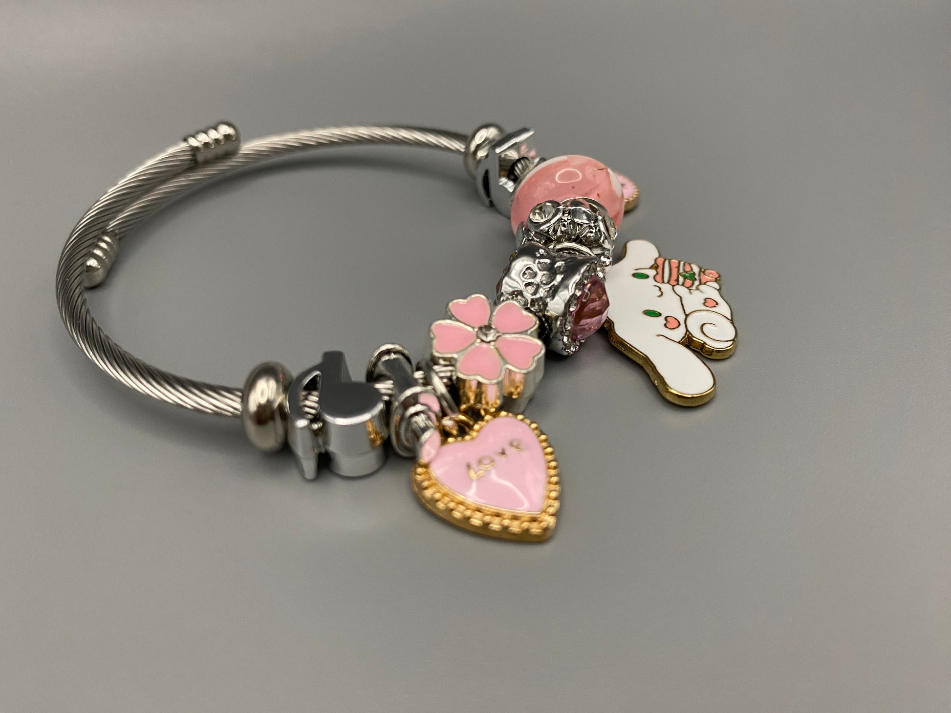 “Cartoon Character Charm Bracelet Bangle in Pink. This charming bracelet features stainless steel bangles adorned with alloy charms, crystals, and glass beads. High-quality materials ensure durability, while the adorable design with pink accents adds a playful elegance. Perfect for everyday wear or special occasions.”