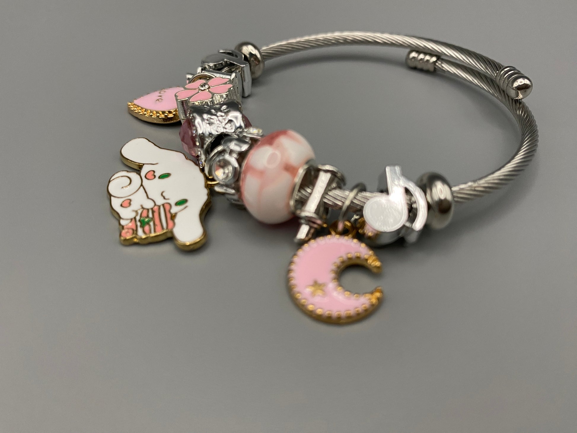 “Cartoon Character Charm Bracelet Bangle in Pink. This charming bracelet features stainless steel bangles adorned with alloy charms, crystals, and glass beads. High-quality materials ensure durability, while the adorable design with pink accents adds a playful elegance. Perfect for everyday wear or special occasions.”