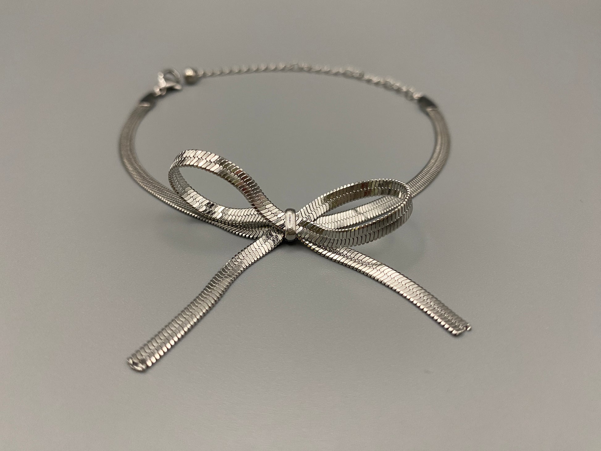 “Celest Angel Bow Bracelet in Silver featuring a delicate bow design, made of stainless steel for durability and tarnish resistance. Measures 18 cm with a 3 cm extender for adjustable fit.”