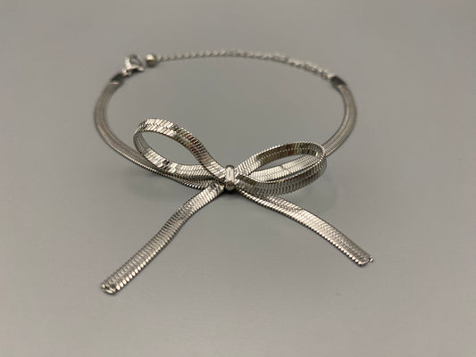 “Celest Angel Bow Bracelet in Silver featuring a delicate bow design, made of stainless steel for durability and tarnish resistance. Measures 18 cm with a 3 cm extender for adjustable fit.”