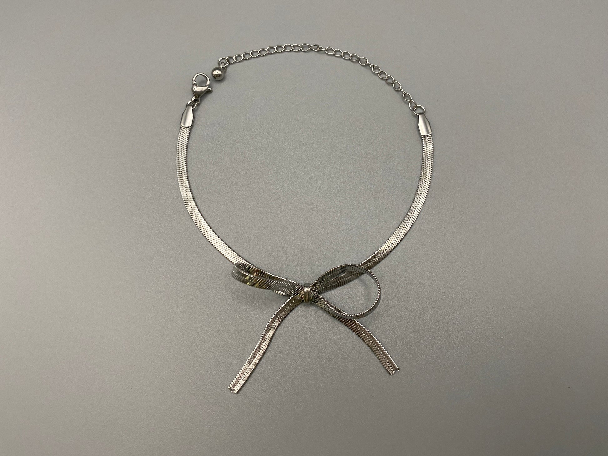 “Celest Angel Bow Bracelet in Silver featuring a delicate bow design, made of stainless steel for durability and tarnish resistance. Measures 18 cm with a 3 cm extender for adjustable fit.”
