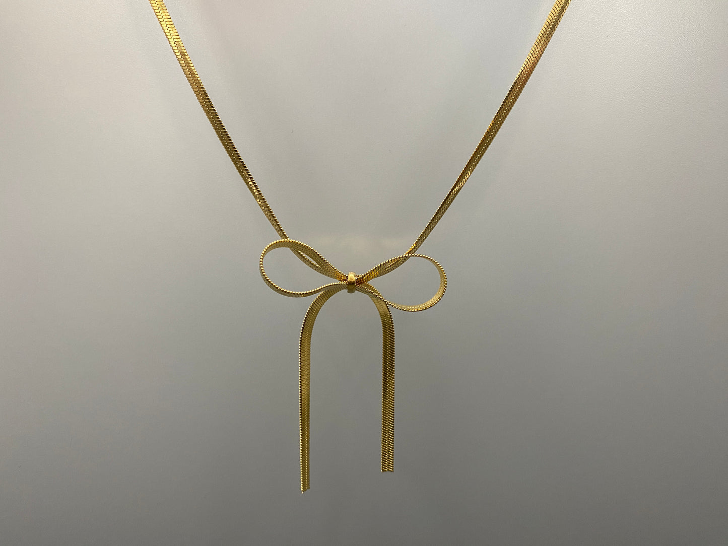 “Celest Angel Bow Pendant Chain in gold with a sophisticated bow pendant design. Made from durable stainless steel, tarnish-free. Measures 35 cm with a 5 cm extender for adjustable fit.”