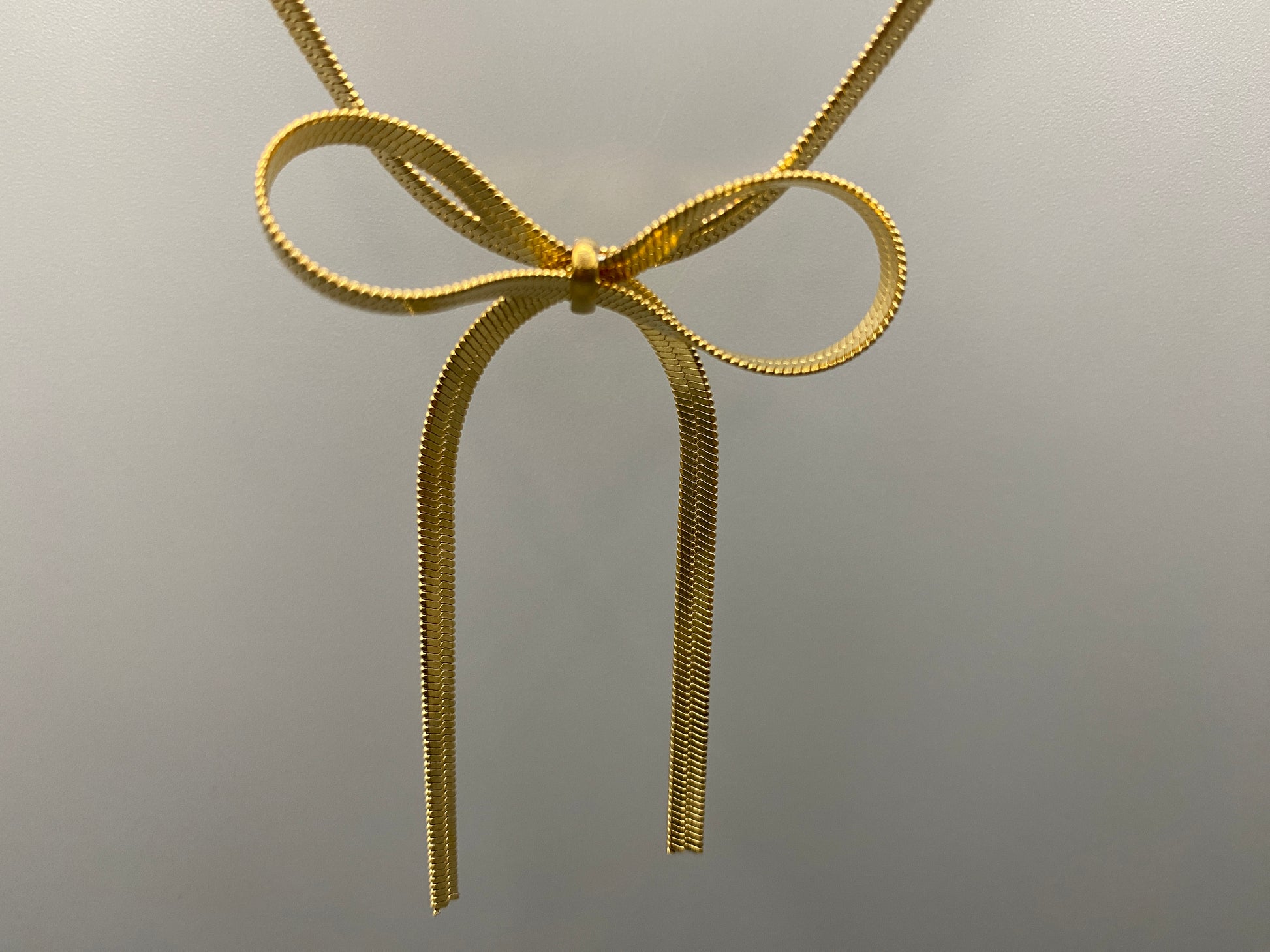 "Celest Angel Bow Pendant Chain in gold features a sophisticated bow pendant design. Crafted from durable stainless steel, it is tarnish-free and measures 35 cm with a 5 cm extender for an adjustable fit."