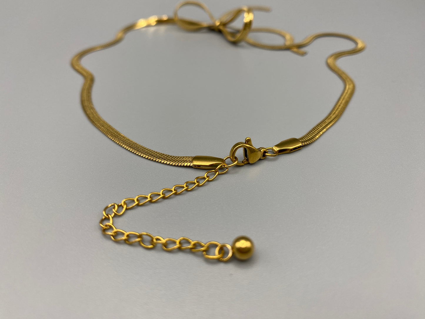 "Celest Angel Bow Pendant Chain in gold features a sophisticated bow pendant design. Crafted from durable stainless steel, it is tarnish-free and measures 35 cm with a 5 cm extender for an adjustable fit."