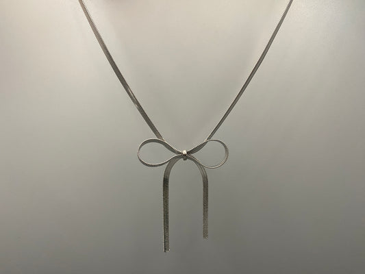 “Celest Angel Bow Pendant Chain in silver with a sophisticated bow pendant design. Made from durable stainless steel, tarnish-free. Measures 35 cm with a 5 cm extender for adjustable fit.”