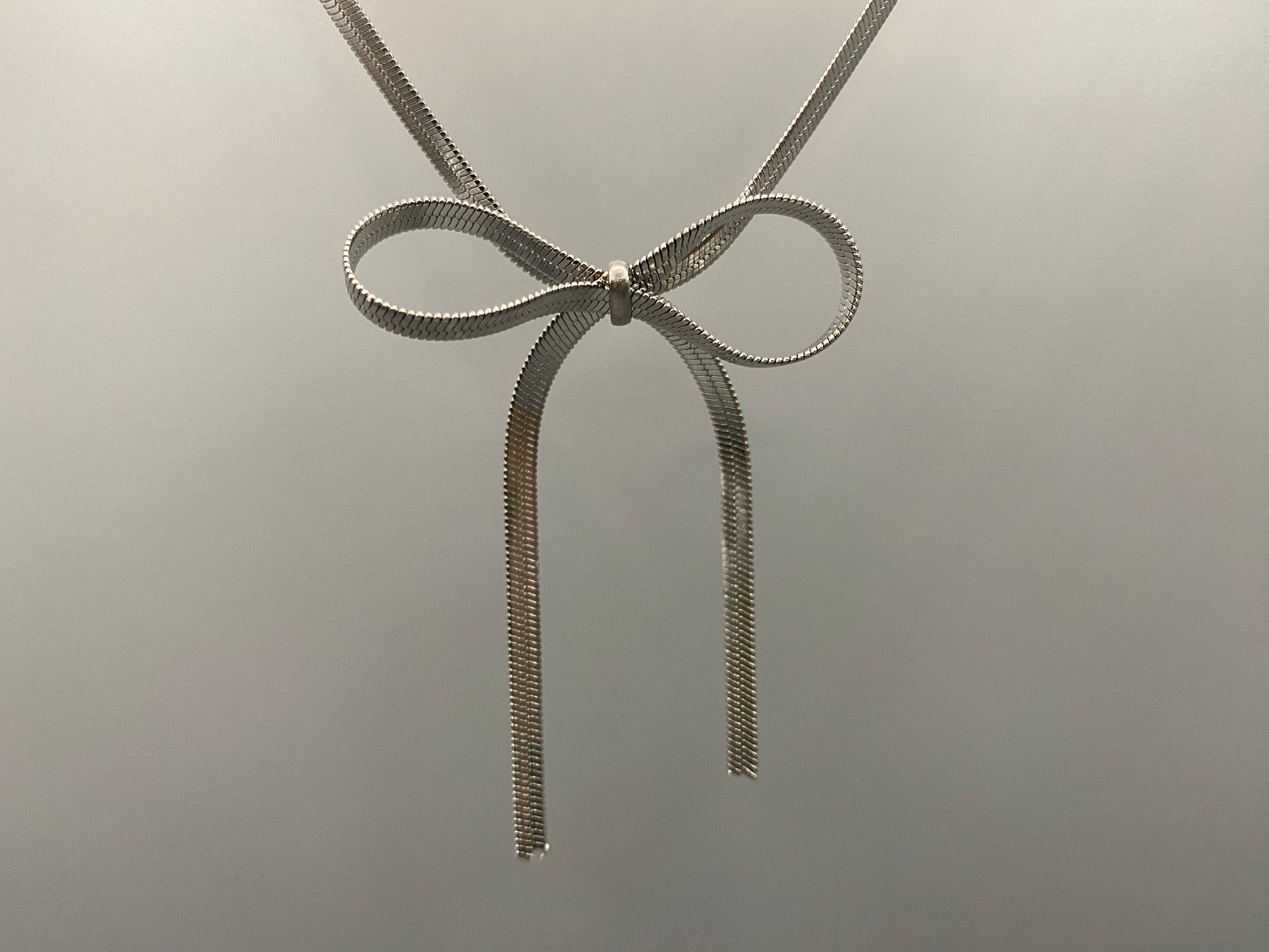 “Celest Angel Bow Pendant Chain in silver with a sophisticated bow pendant design. Made from durable stainless steel, tarnish-free. Measures 35 cm with a 5 cm extender for adjustable fit.”