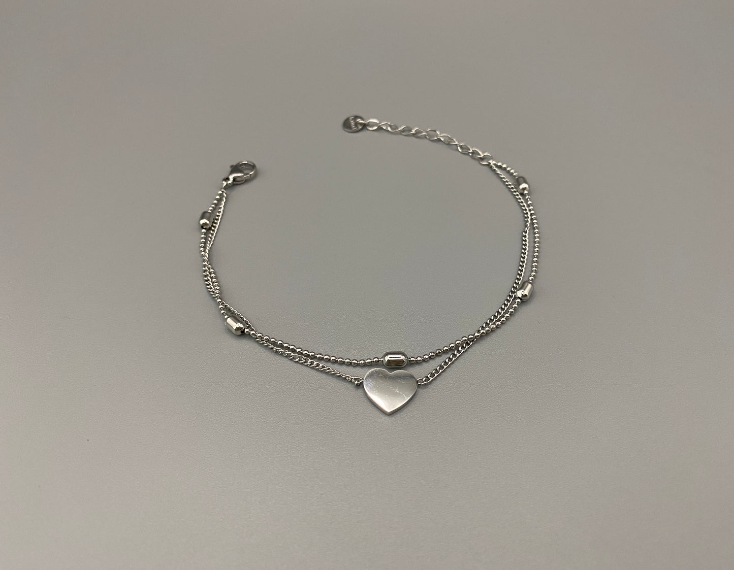 “Cora Twin Chain Heart and Bead Bracelet in gold, featuring a romantic twin chain design with heart and bead accents. silver plated, made from durable titanium steel with PVD plating. Measures 17 cm with a 3 cm extender for adjustable fit.”