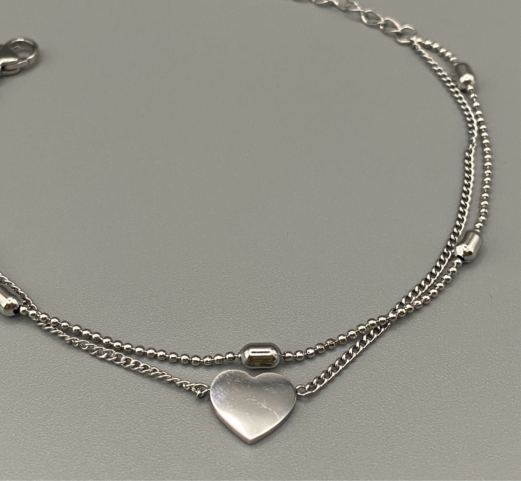 “Cora Twin Chain Heart and Bead Bracelet in gold, featuring a romantic twin chain design with heart and bead accents. silver plated, made from durable titanium steel with PVD plating. Measures 17 cm with a 3 cm extender for adjustable fit.”