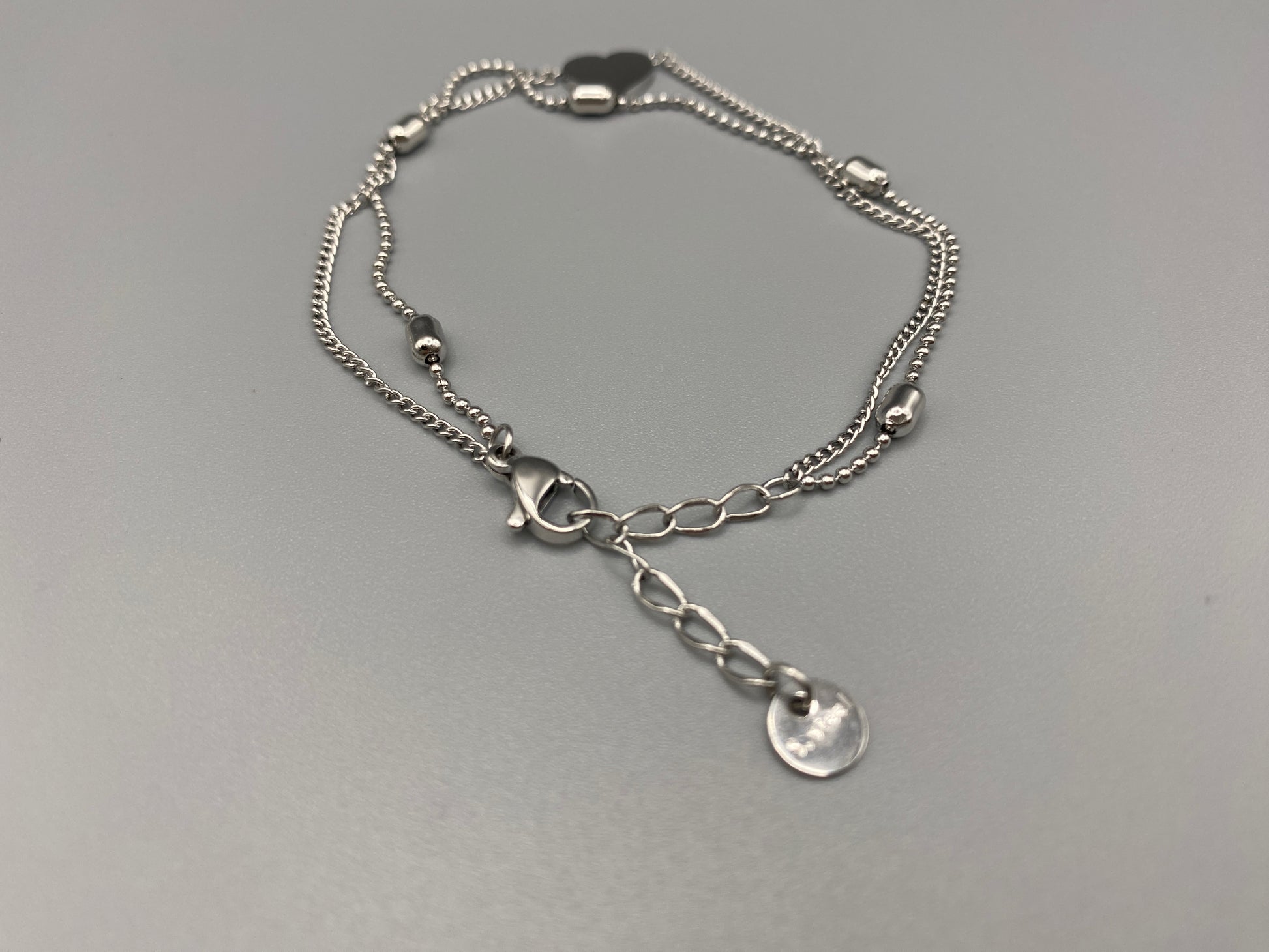 “Cora Twin Chain Heart and Bead Bracelet in gold, featuring a romantic twin chain design with heart and bead accents. silver plated, made from durable titanium steel with PVD plating. Measures 17 cm with a 3 cm extender for adjustable fit.”
