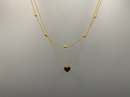 Cora, This exquisite necklace is crafted from luxurious 18K gold, featuring a unique twin chain design. One chain is adorned with delicate beads, while the other showcases a charming heart-shaped pendant.