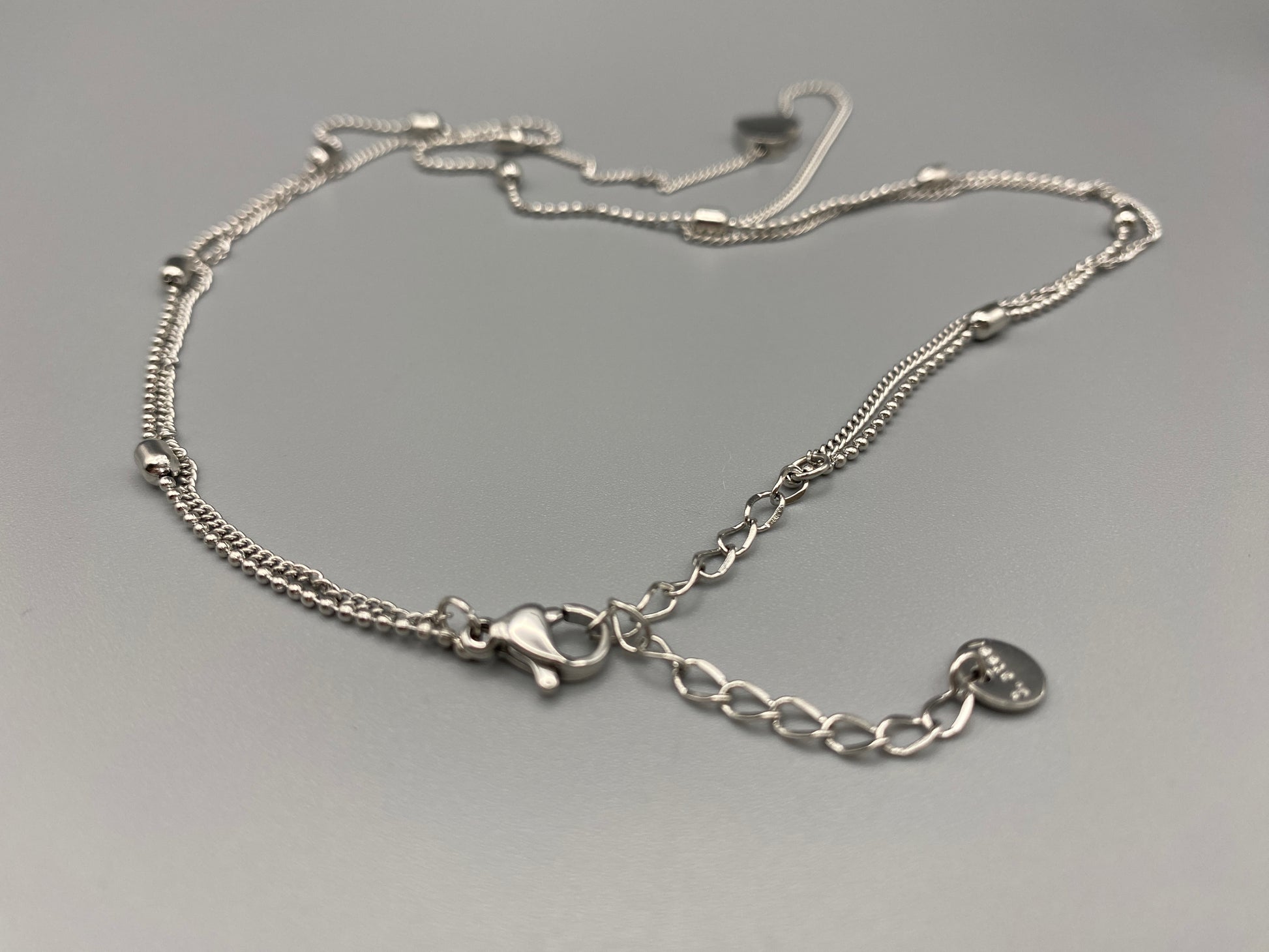 Cora Twin Chain Heart and Bead Necklace in Silver. Features: Durable Material: Crafted from stainless steel, known for its strength and resistance to tarnish. Elegant Design: The twin chain design with beads and heart elements adds a touch of sophistication. Adjustable Length: Measures 41 cm with an additional 5 cm extension for a customizable and comfortable fit. PVD Plating: Provides enhanced durability and resistance to wear, ensuring lasting beauty.