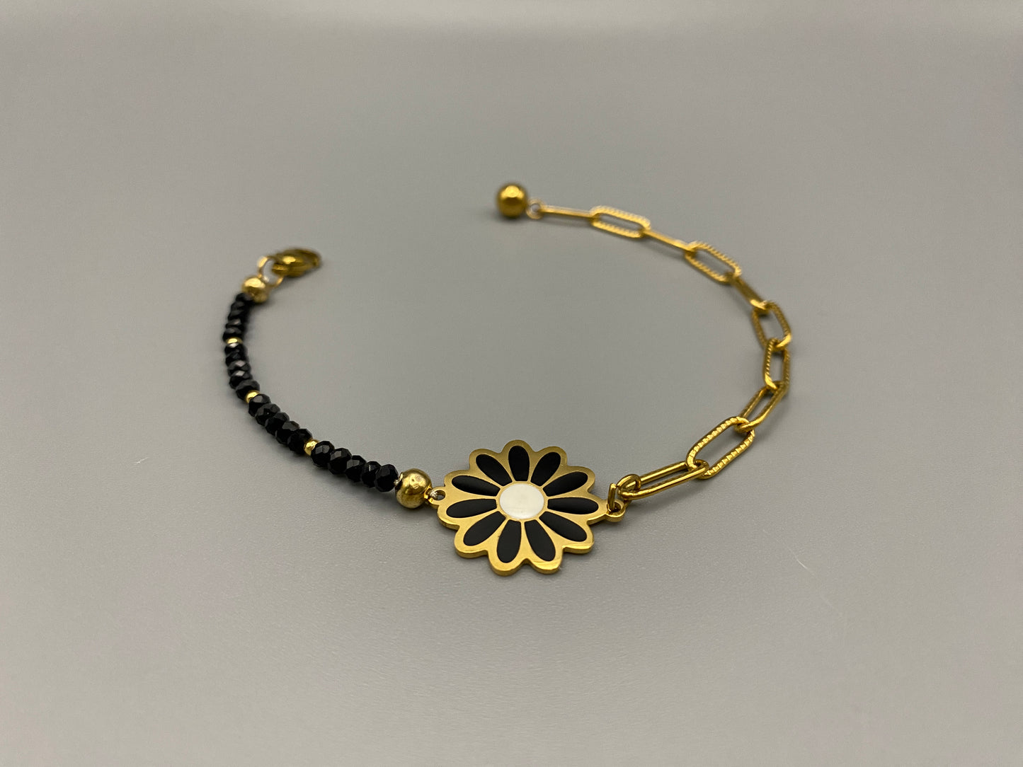 “Daisy Chain Bead Bracelet in black, crafted from stainless steel with 18K gold plating. Features a daisy flower pattern with crystal and rhinestone accents. Eco-friendly, nickel and lead-free, safe for sensitive skin.”