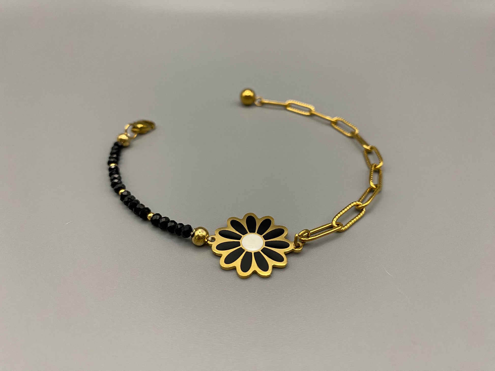 “Daisy Chain Bead Bracelet in black, crafted from stainless steel with 18K gold plating. Features a daisy flower pattern with crystal and rhinestone accents. Eco-friendly, nickel and lead-free, safe for sensitive skin.”