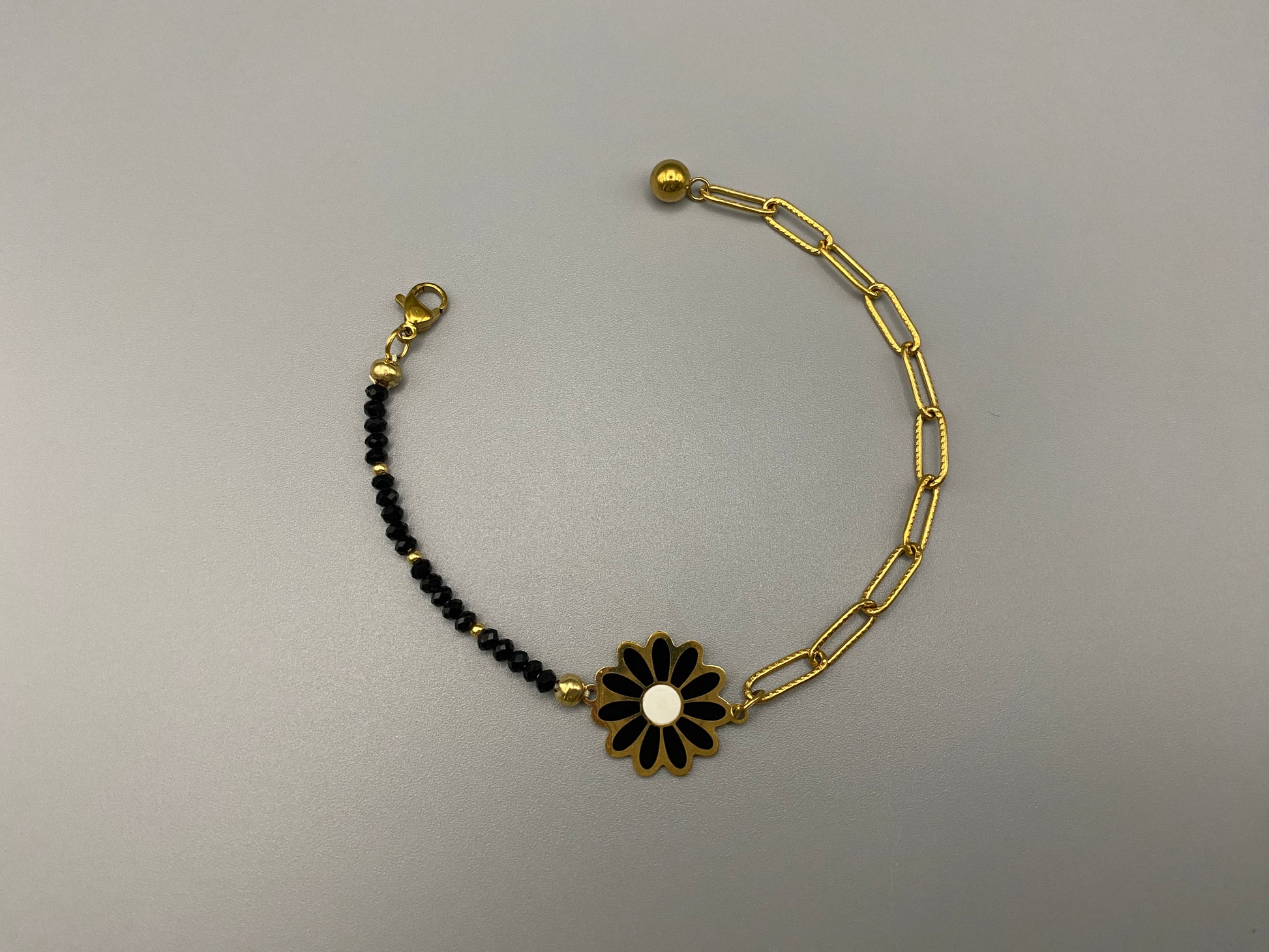 “Daisy Chain Bead Bracelet in black, crafted from stainless steel with 18K gold plating. Features a daisy flower pattern with crystal and rhinestone accents. Eco-friendly, nickel and lead-free, safe for sensitive skin.”