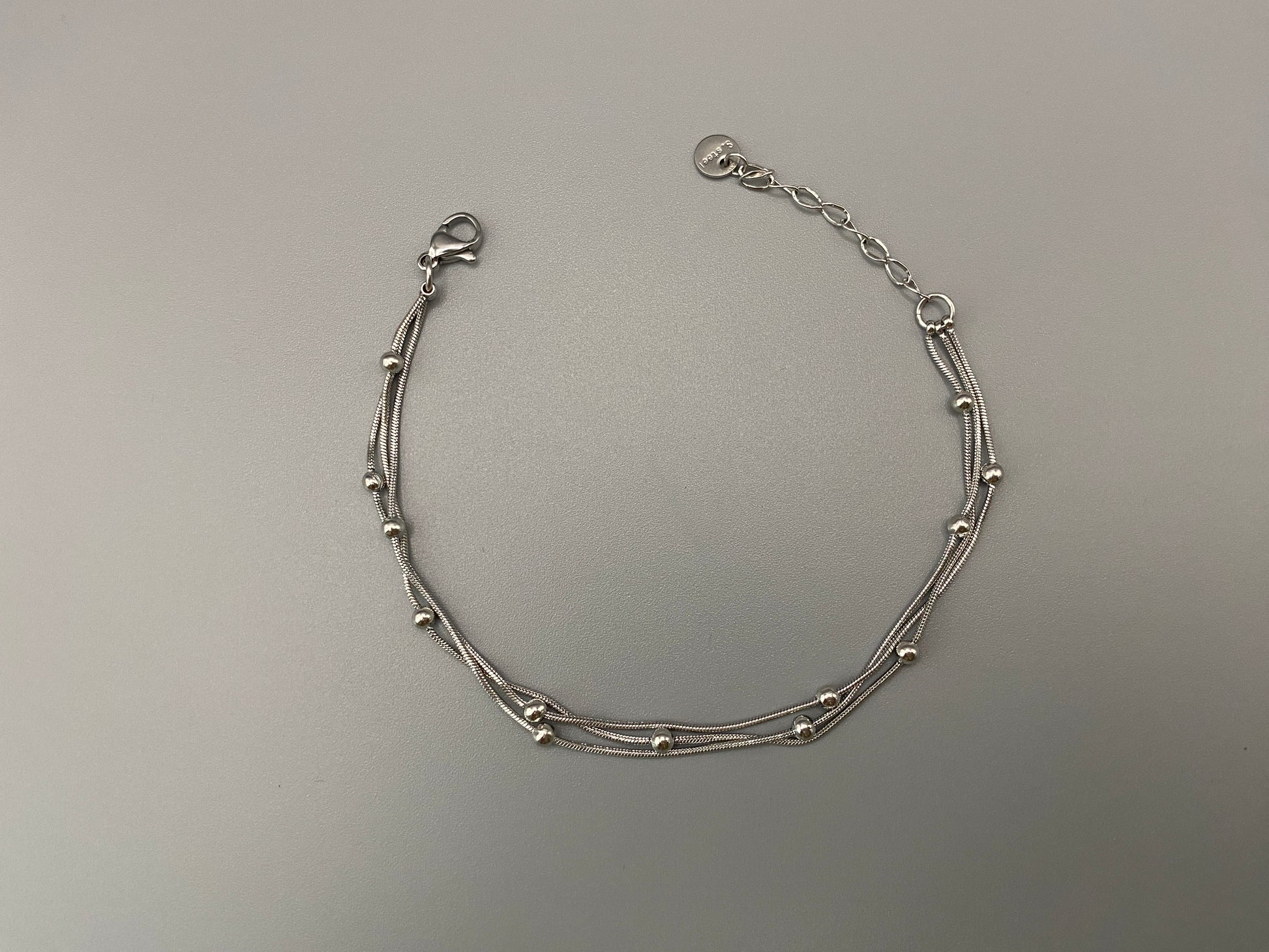 “Freya Tri-Chained Bead Bracelet in silver with three delicate chains and evenly spaced small beads. Silver plated, made from durable stainless steel with PVD plating. Measures 18 cm with a 3 cm extender for adjustable fit.”