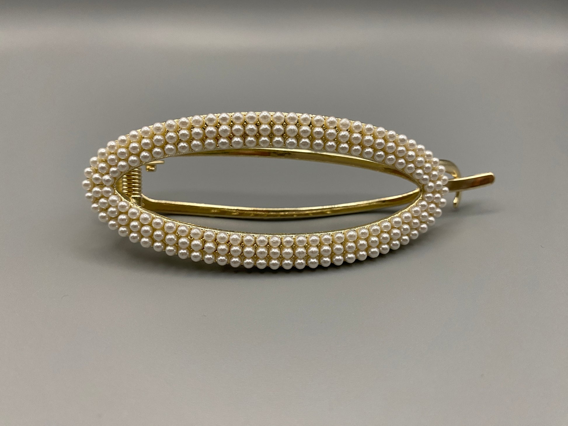  “GlitzGrip hair accessory with a hollow oval design, adorned with pearl inlayed gems and a gold finish, measuring 9.5 cm in length for a secure hold.”