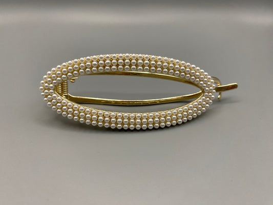  “GlitzGrip hair accessory with a hollow oval design, adorned with pearl inlayed gems and a gold finish, measuring 9.5 cm in length for a secure hold.”
