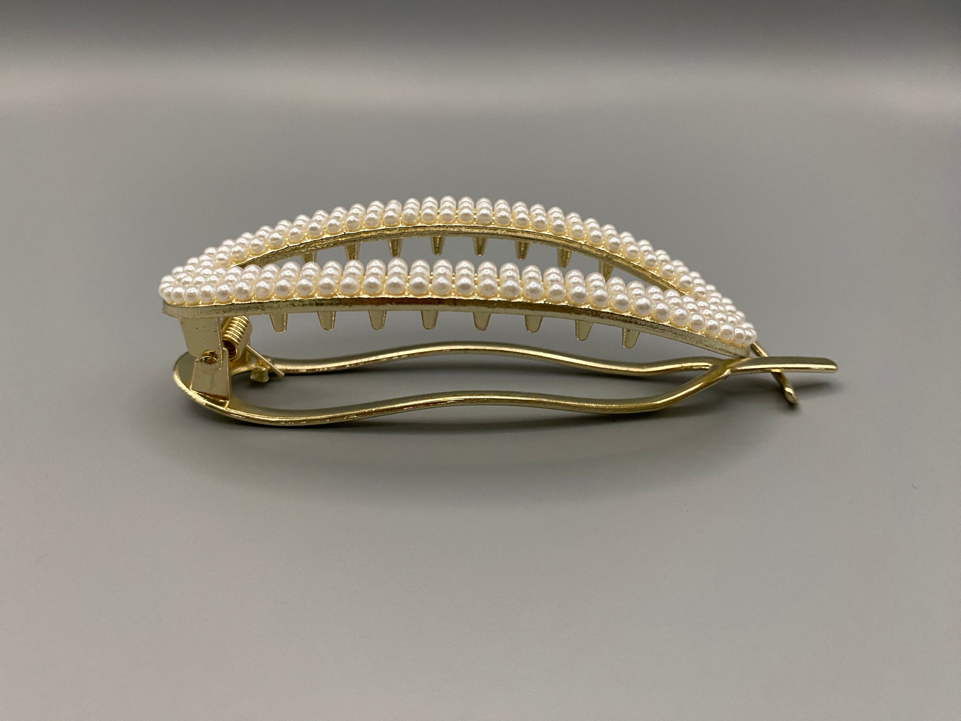  “GlitzGrip hair accessory with a hollow oval design, adorned with pearl inlayed gems and a gold finish, measuring 9.5 cm in length for a secure hold.”