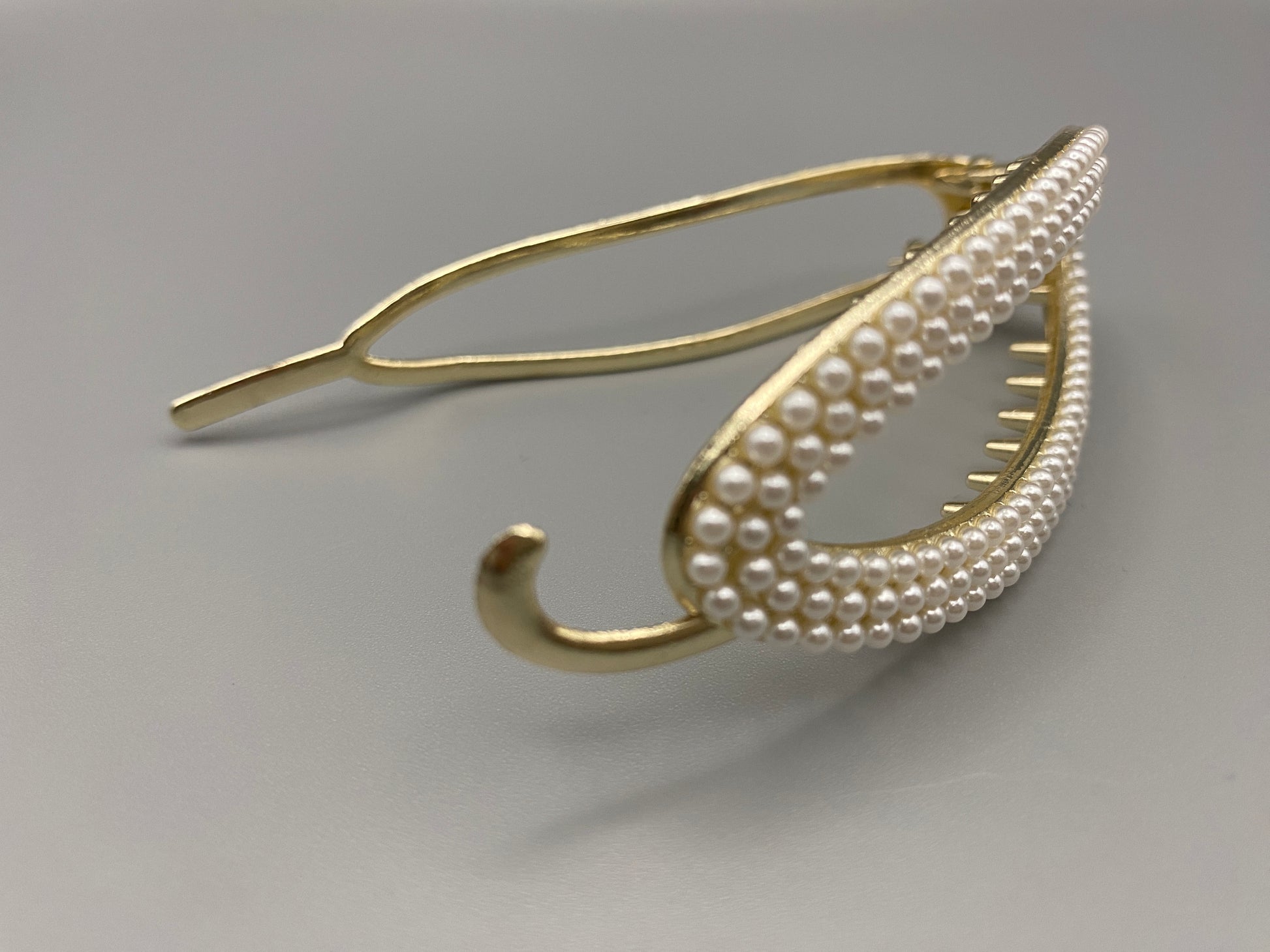  “GlitzGrip hair accessory with a hollow oval design, adorned with pearl inlayed gems and a gold finish, measuring 9.5 cm in length for a secure hold.”