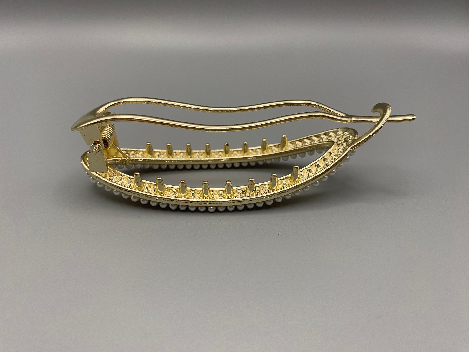  “GlitzGrip hair accessory with a hollow oval design, adorned with pearl inlayed gems and a gold finish, measuring 9.5 cm in length for a secure hold.”