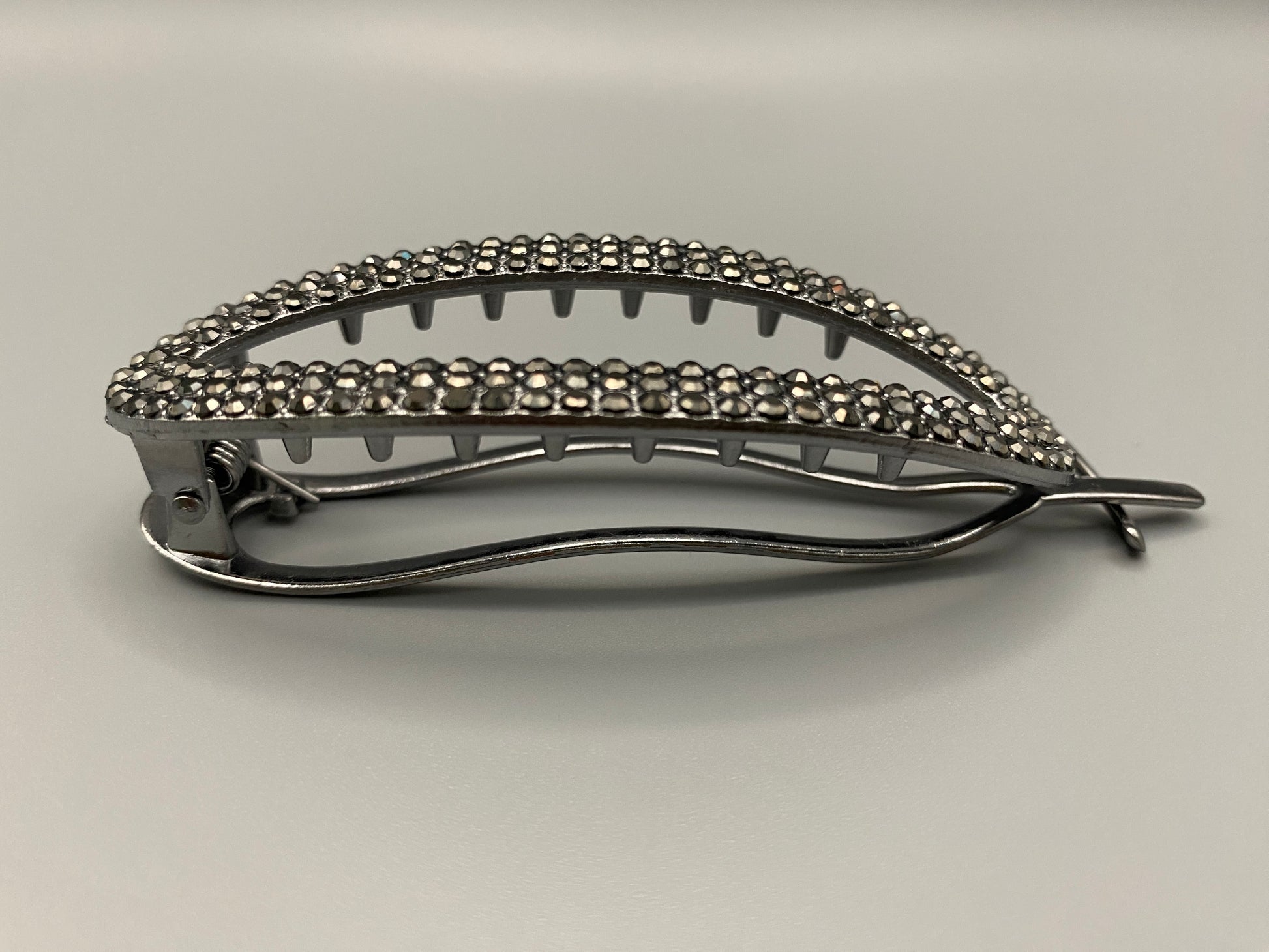 “GlitzGrip Oval Hollow Silver Hair Clip with a hollow oval design, encrusted with sparkling zircon gems. Measures 9.5 cm in length, offering a secure hold for various hair types and styles. Elegant and durable, perfect for both casual and formal hairstyles.”