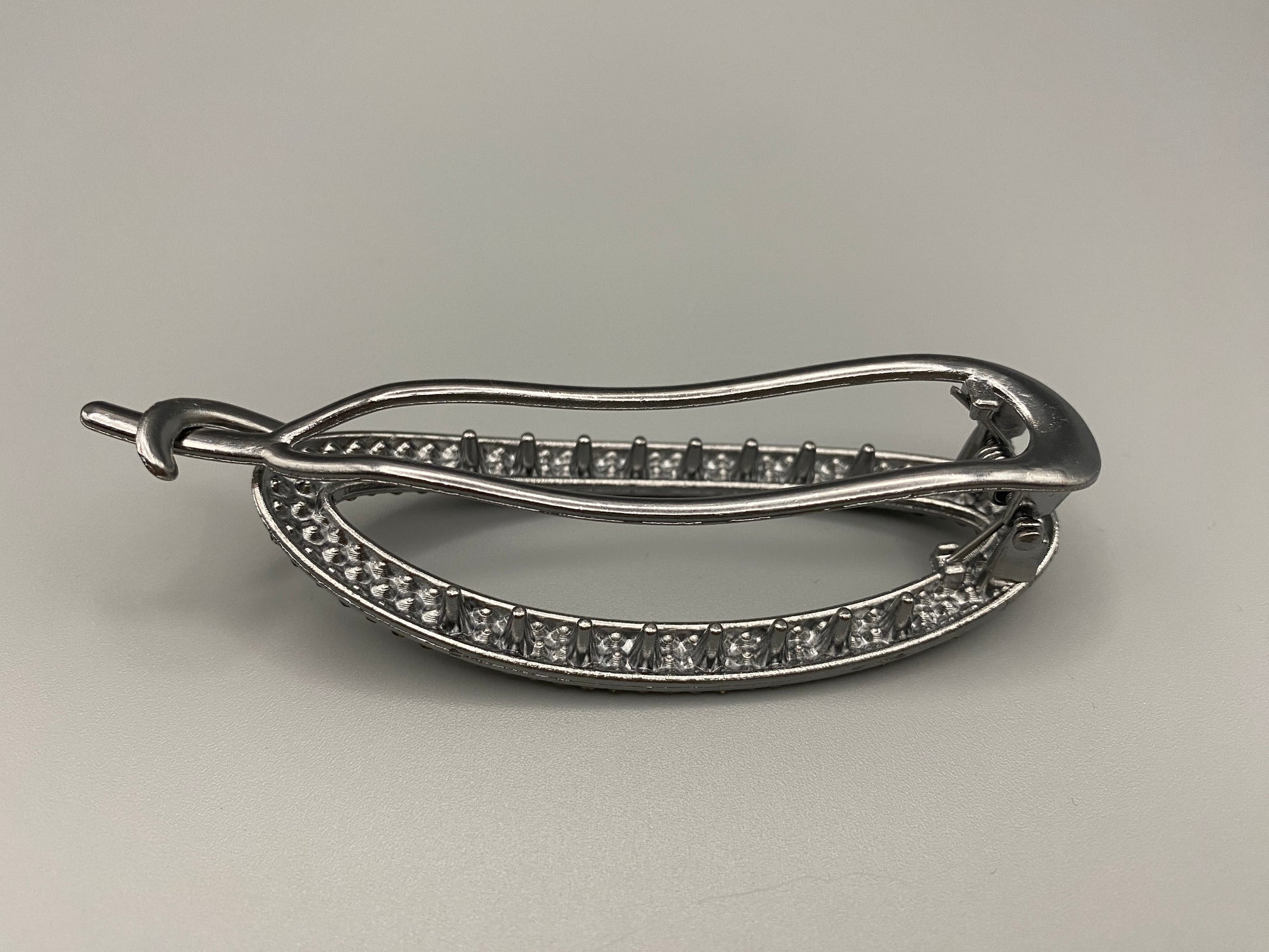 “GlitzGrip Oval Hollow Silver Hair Clip with a hollow oval design, encrusted with sparkling zircon gems. Measures 9.5 cm in length, offering a secure hold for various hair types and styles. Elegant and durable, perfect for both casual and formal hairstyles.”