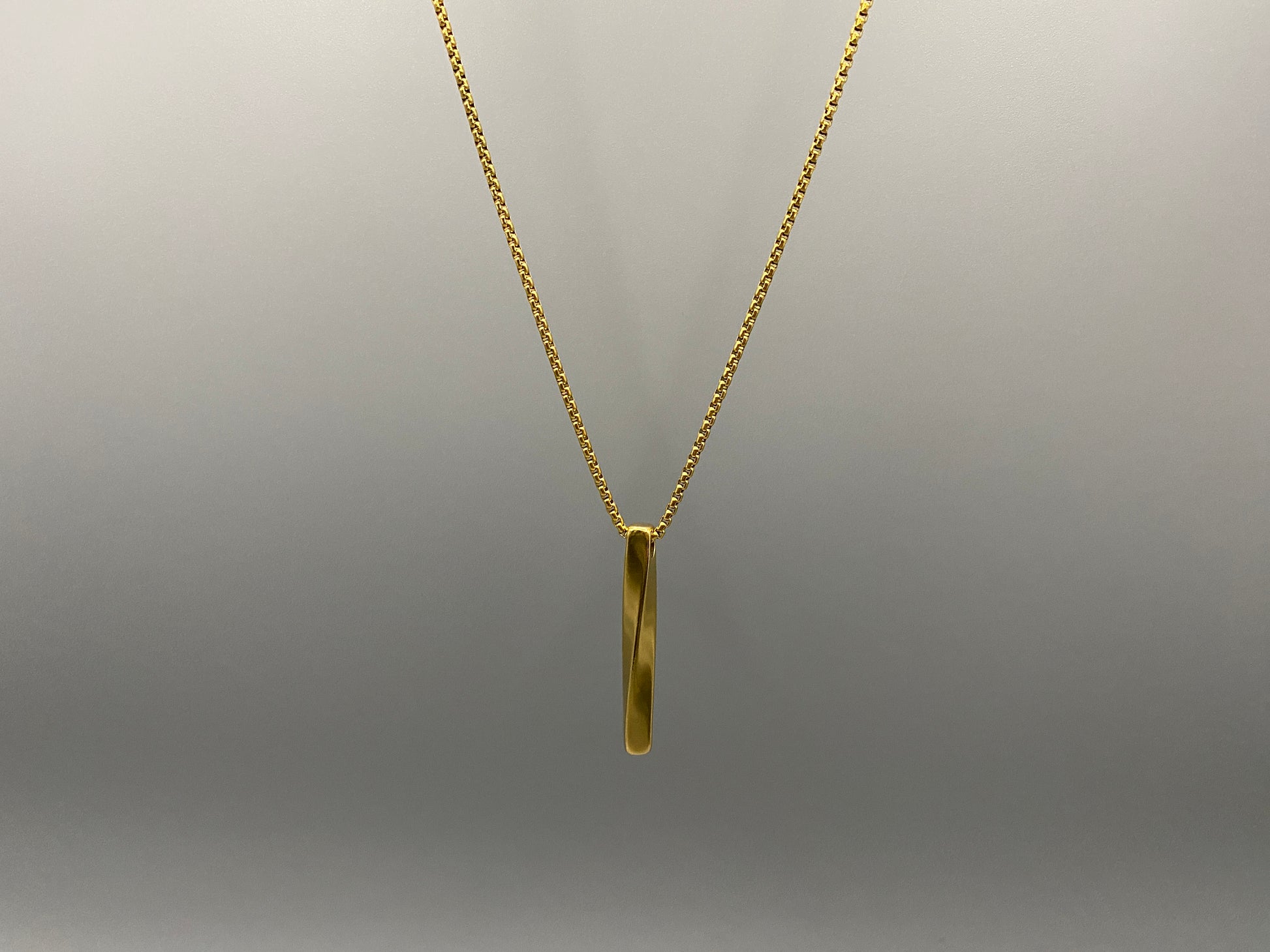 “Three stainless steel twist pendant necklaces in black gun plated, gold plated, and titanium plated finishes, displayed on a dark background. Each necklace features a geometric twist pendant on a link chain, suitable for unisex wear.”