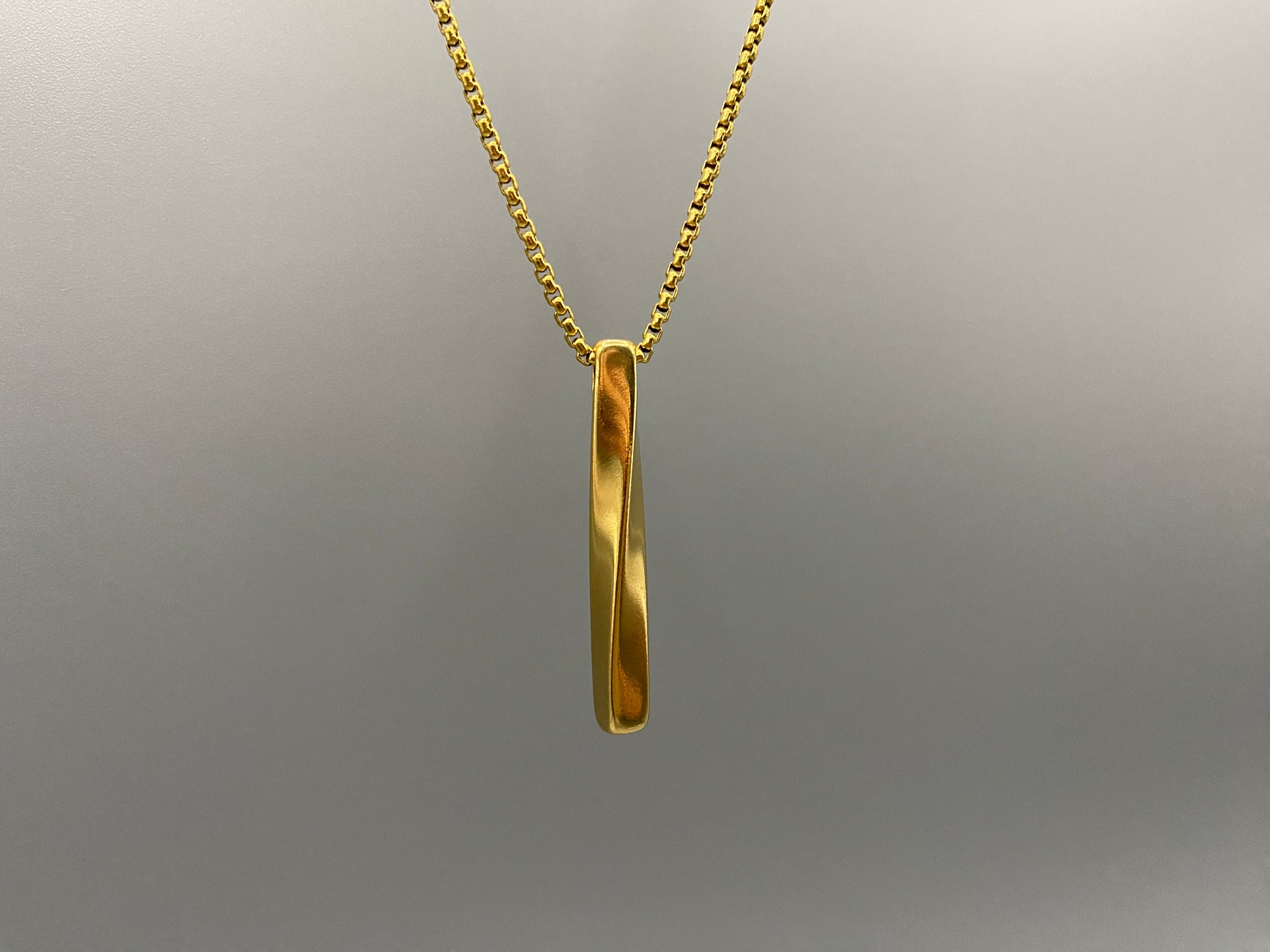 “Three stainless steel twist pendant necklaces in black gun plated, gold plated, and titanium plated finishes, displayed on a dark background. Each necklace features a geometric twist pendant on a link chain, suitable for unisex wear.”