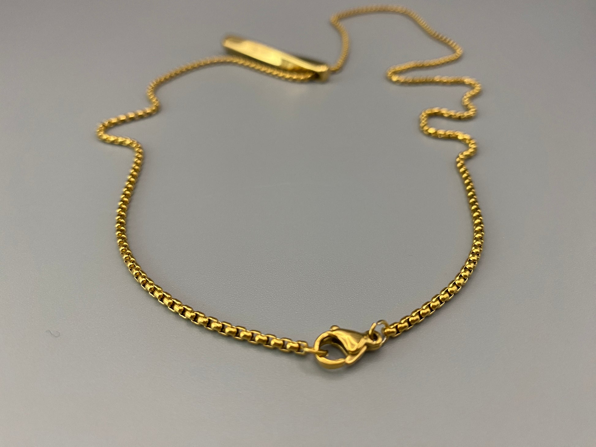 “Three stainless steel twist pendant necklaces in black gun plated, gold plated, and titanium plated finishes, displayed on a dark background. Each necklace features a geometric twist pendant on a link chain, suitable for 