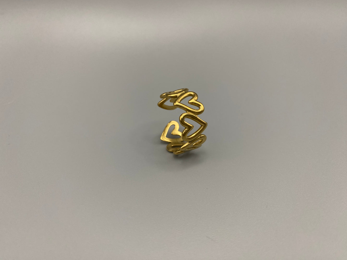 Ring Of Hearts Gold: Embrace elegance and modernity with our Ring of Hearts. Crafted from high-quality stainless steel and plated with 18K gold, this trendy geometric ring features interconnected hearts. Symbolizing unity and love, this adjustable ring is a versatile accessory for any occasion.
