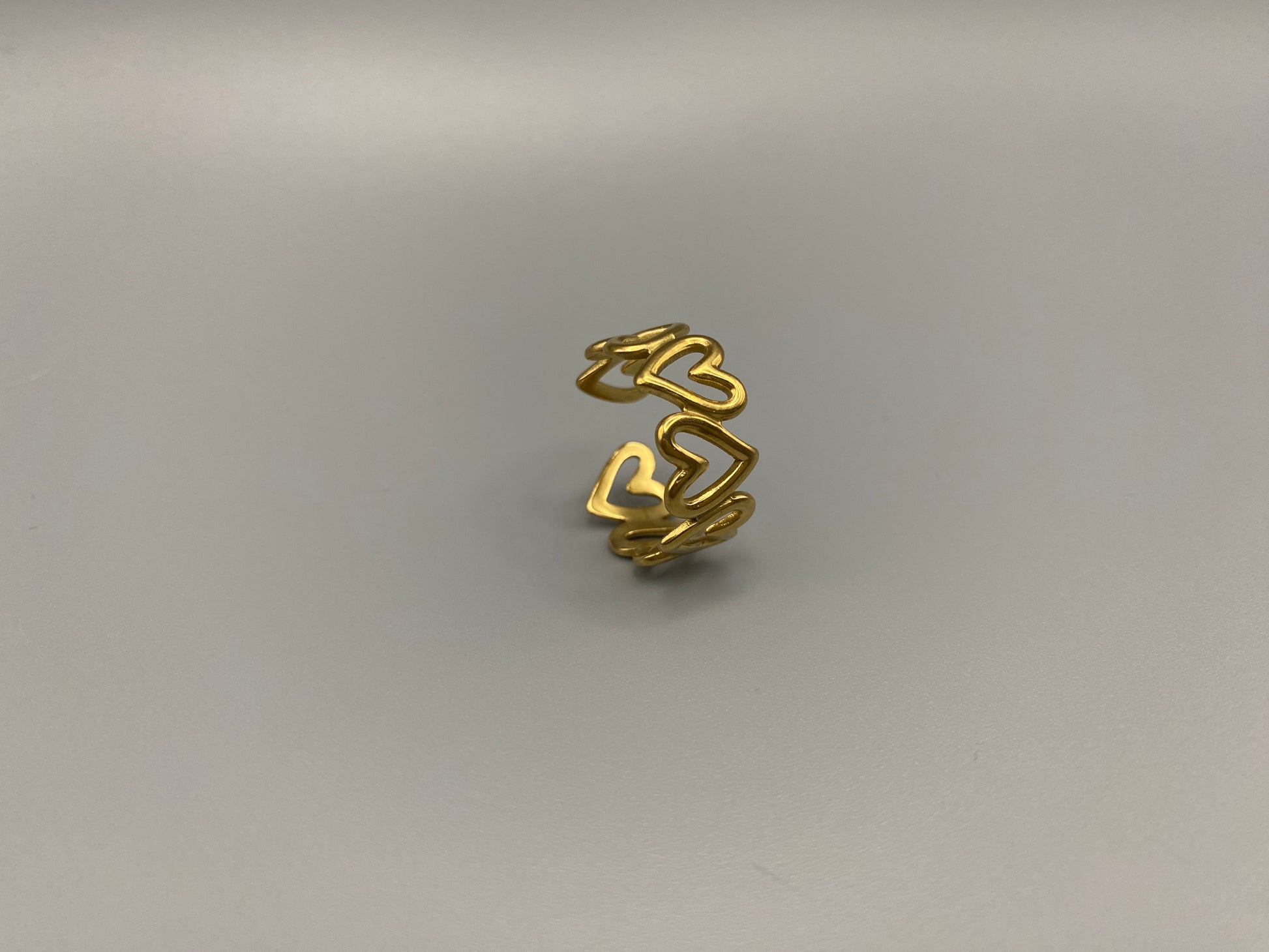 Ring Of Hearts Gold: Embrace elegance and modernity with our Ring of Hearts. Crafted from high-quality stainless steel and plated with 18K gold, this trendy geometric ring features interconnected hearts. Symbolizing unity and love, this adjustable ring is a versatile accessory for any occasion.