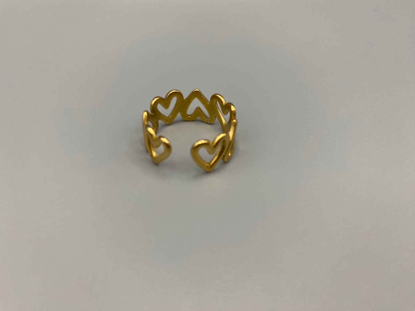 Ring Of Hearts Gold: Embrace elegance and modernity with our Ring of Hearts. Crafted from high-quality stainless steel and plated with 18K gold, this trendy geometric ring features interconnected hearts. Symbolizing unity and love, this adjustable ring is a versatile accessory for any occasion.
