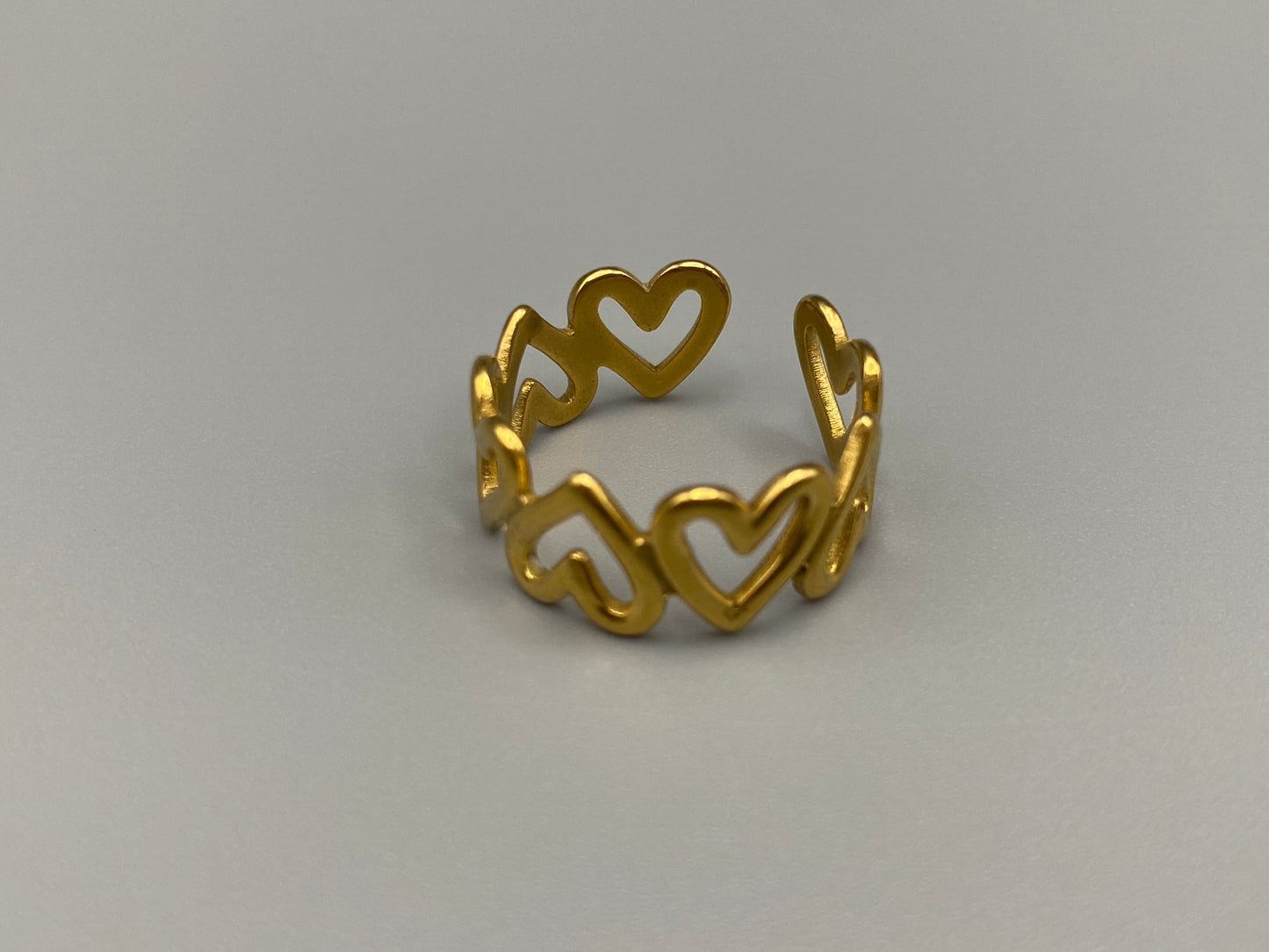 Ring Of Hearts Gold: Embrace elegance and modernity with our Ring of Hearts. Crafted from high-quality stainless steel and plated with 18K gold, this trendy geometric ring features interconnected hearts. Symbolizing unity and love, this adjustable ring is a versatile accessory for any occasion.
