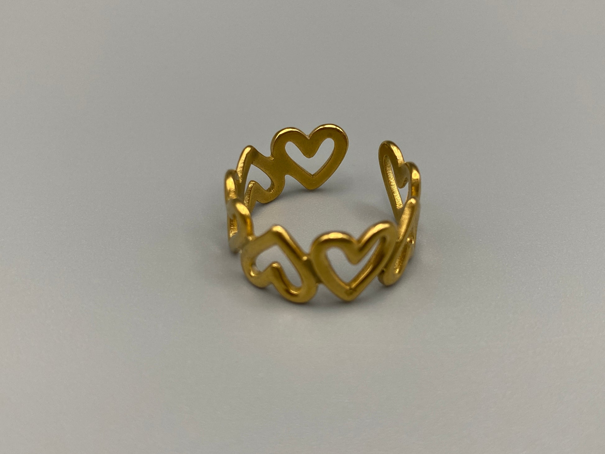 Ring Of Hearts Gold: Embrace elegance and modernity with our Ring of Hearts. Crafted from high-quality stainless steel and plated with 18K gold, this trendy geometric ring features interconnected hearts. Symbolizing unity and love, this adjustable ring is a versatile accessory for any occasion.