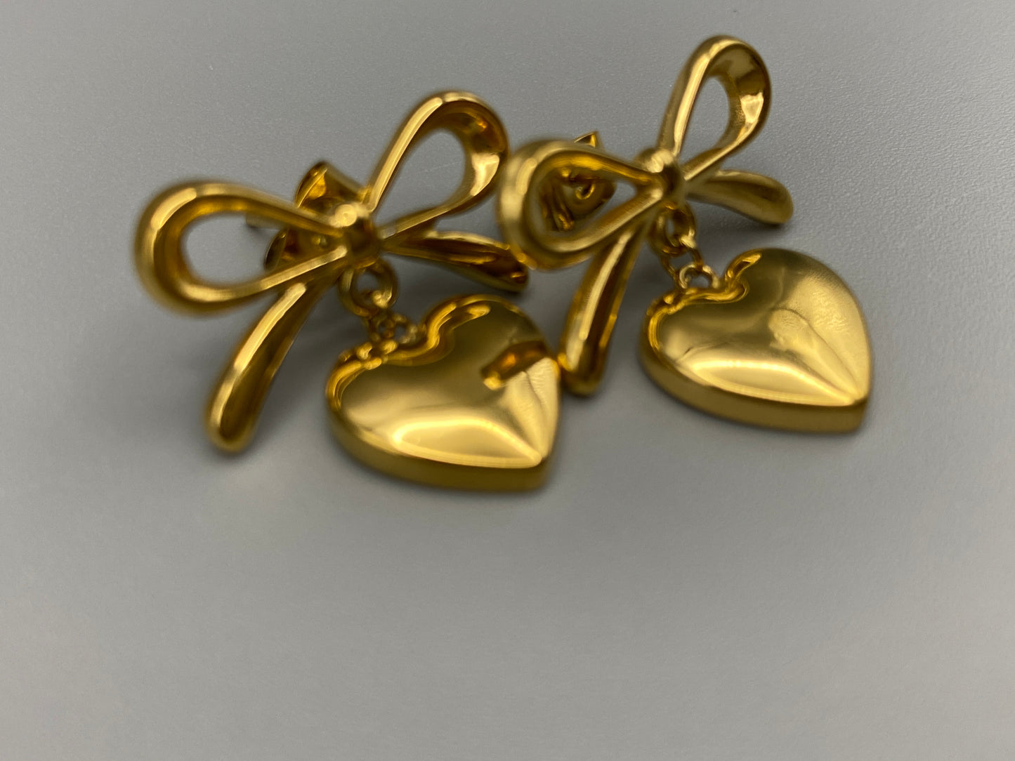 “Tanya Heart Bow Earrings Gold: Elegant and modern heart-shaped pendant adorned with a delicate bow, crafted from high-quality stainless steel and plated with 18K gold. Waterproof, tarnish-free, and environmentally friendly, perfect for daily wear or special occasions.”
