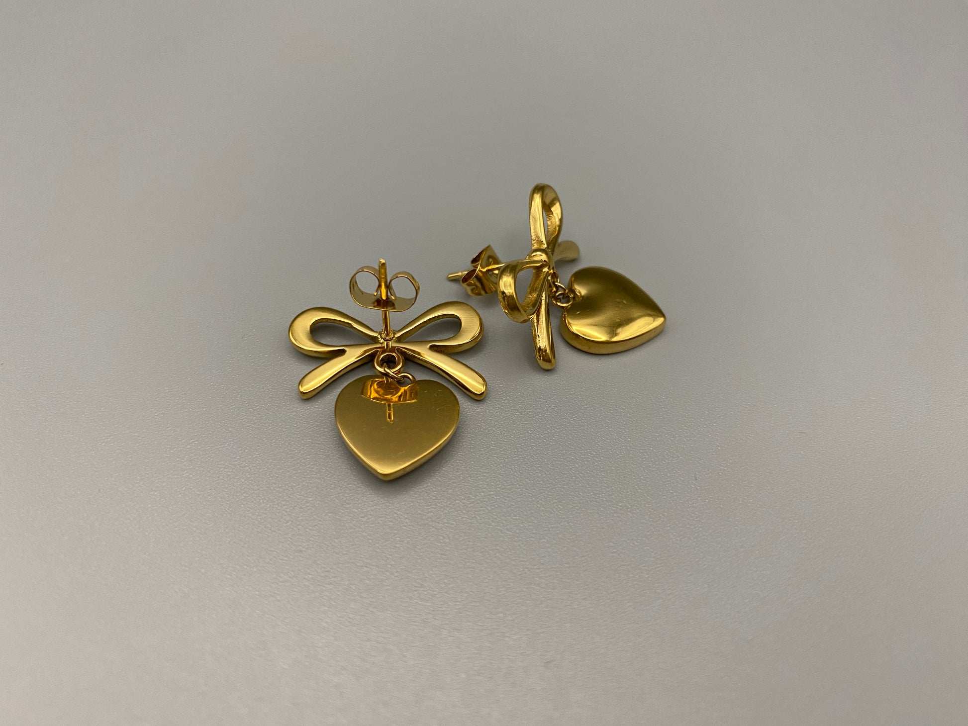 “Tanya Heart Bow Earrings Gold: Elegant and modern heart-shaped pendant adorned with a delicate bow, crafted from high-quality stainless steel and plated with 18K gold. Waterproof, tarnish-free, and environmentally friendly, perfect for daily wear or special occasions.”