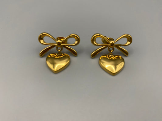 “Tanya Heart Bow Earrings Gold: Elegant and modern heart-shaped pendant adorned with a delicate bow, crafted from high-quality stainless steel and plated with 18K gold. Waterproof, tarnish-free, and environmentally friendly, perfect for daily wear or special occasions.”