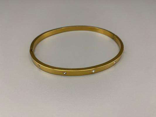 “Lucy Bangle in Gold with 18K gold plating, featuring a gemstone inlay for added elegance and sparkle. This durable bangle ensures long-lasting wear and resistance to tarnish. Its sophisticated design makes it perfect for both everyday wear and special occasions, adding a touch of glamour to any look.”